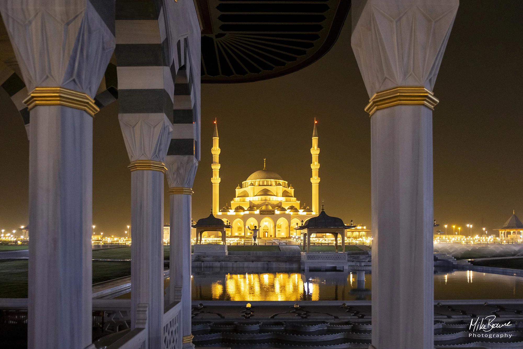 Distant man raising his arms at floodlit Sharjah Mosque, UAE