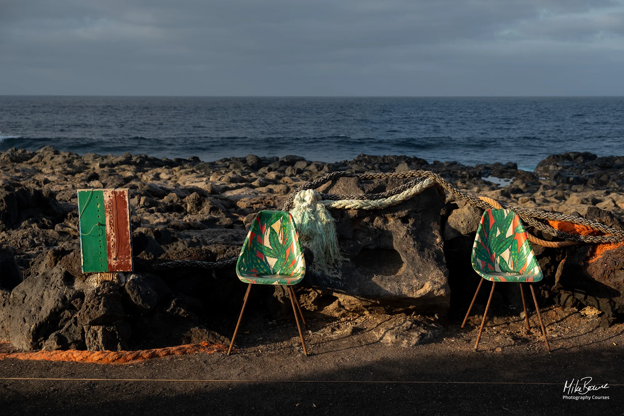 Two green patterned chairs and mooring rope catch sunlight by the sea in Tenesar, Lanzarote
