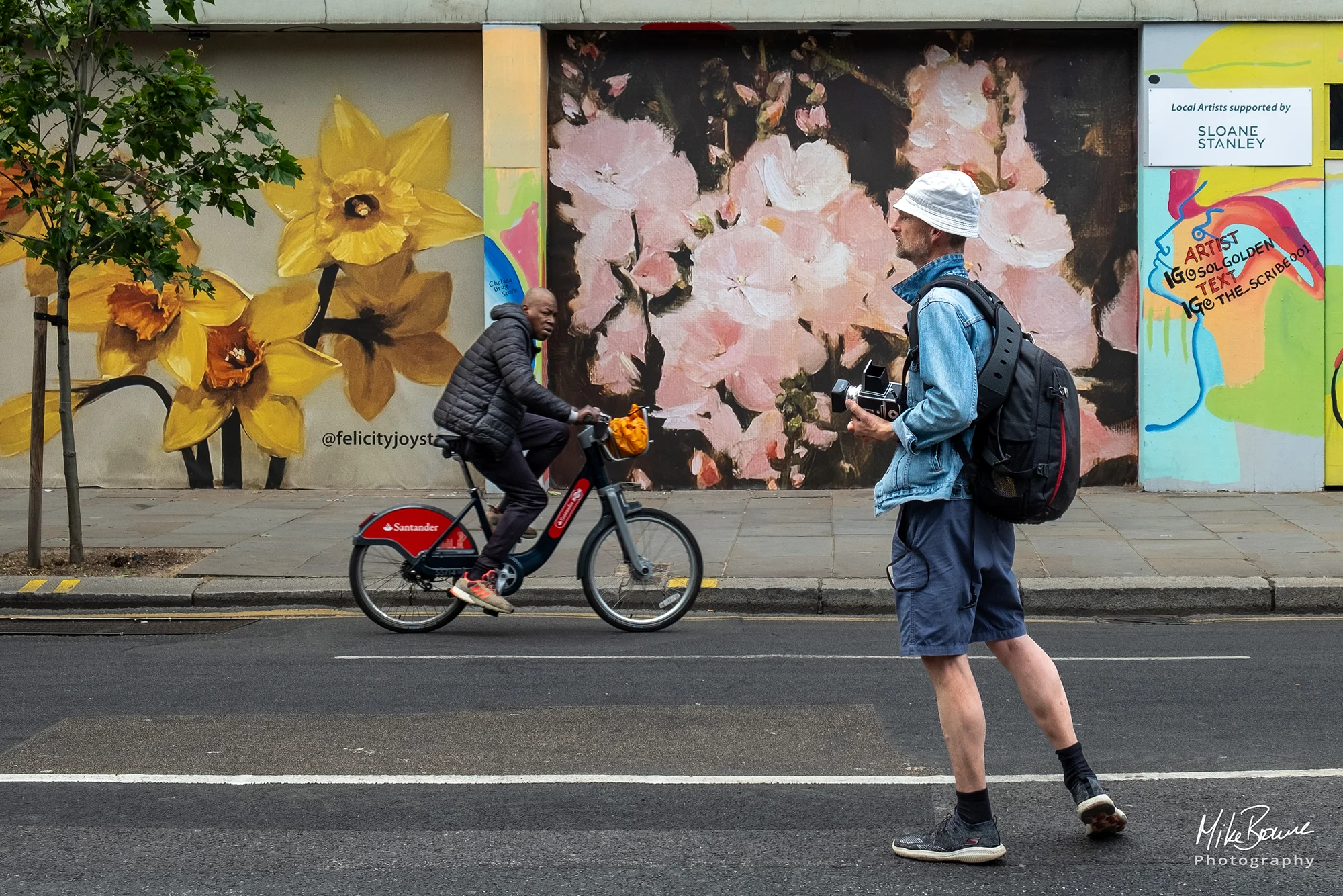 Photographer standing in street as man ob bicycle rides by looking at him