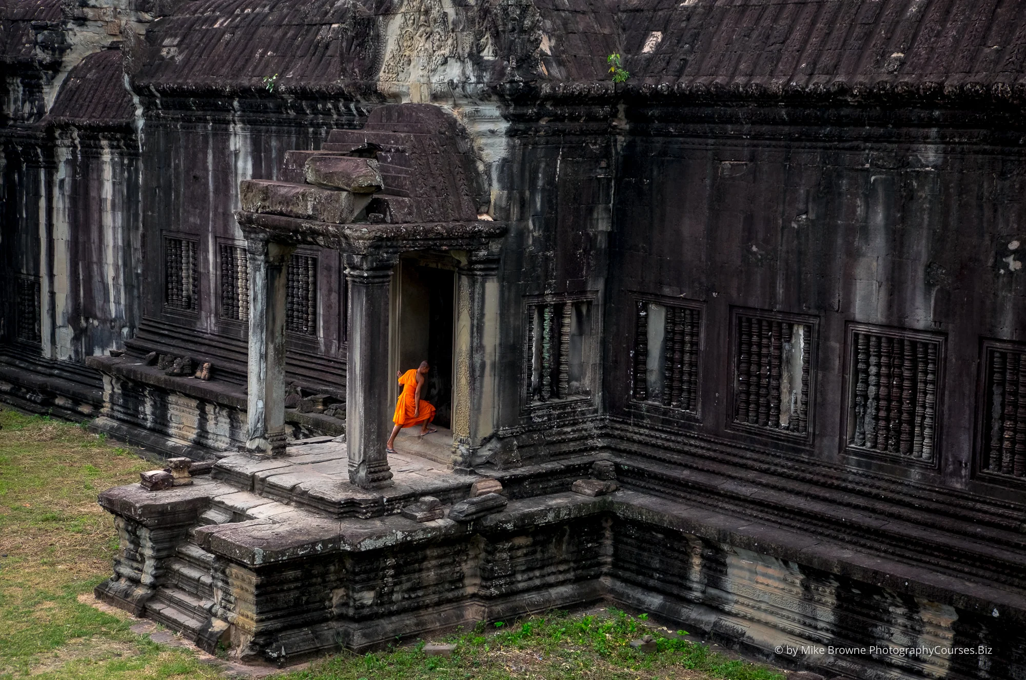 Monk wearing orange robes entering Angkor Watt temple in Cambodia