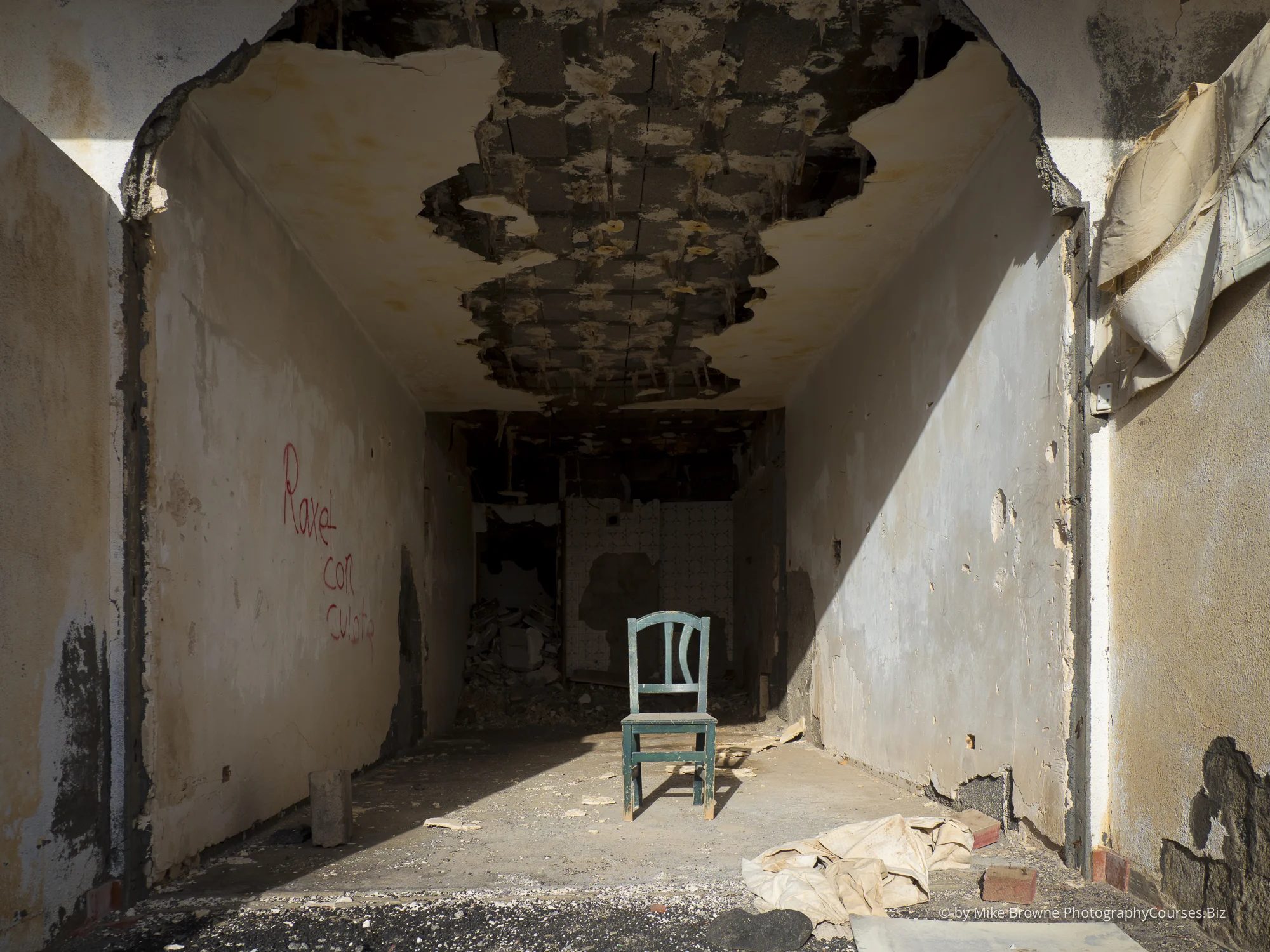 Green chair and diagonal shadow amidst ruins of abandoned hotel