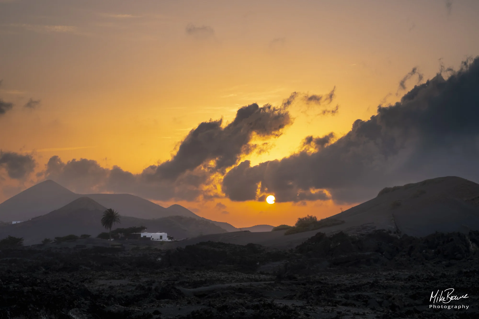 Sunset over house and lone palm tree amongst black volcanic rocks on Lanzarote