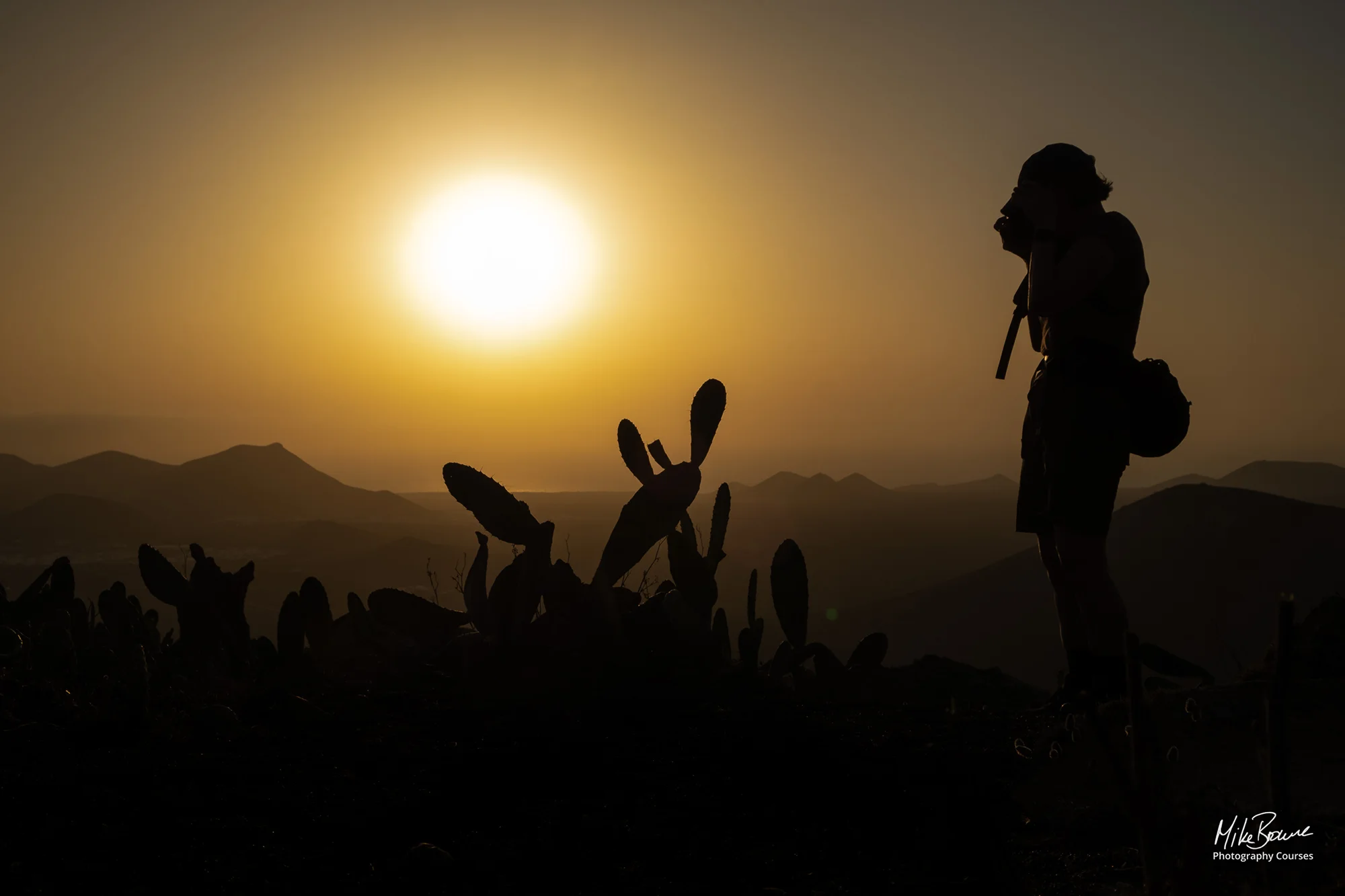 Woman surrounded by cactuses photographing sunset in mountains on Lanzarote