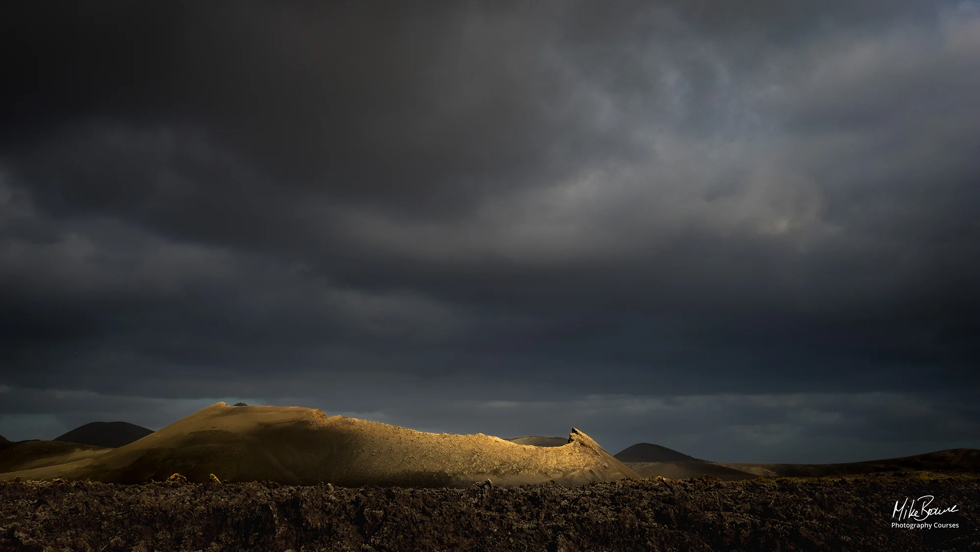 Sunlight catching rim of an old volcano in lava field on a stormy day