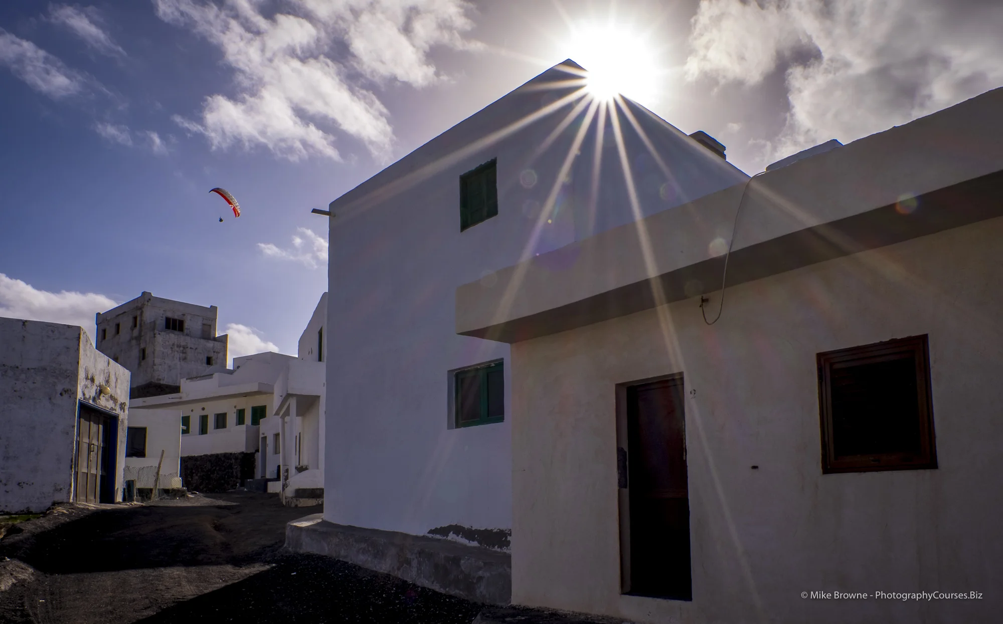 Sun catching corner of a white house and a distant red hang glider in a clear blue sky in Tenesar, Lanzarote