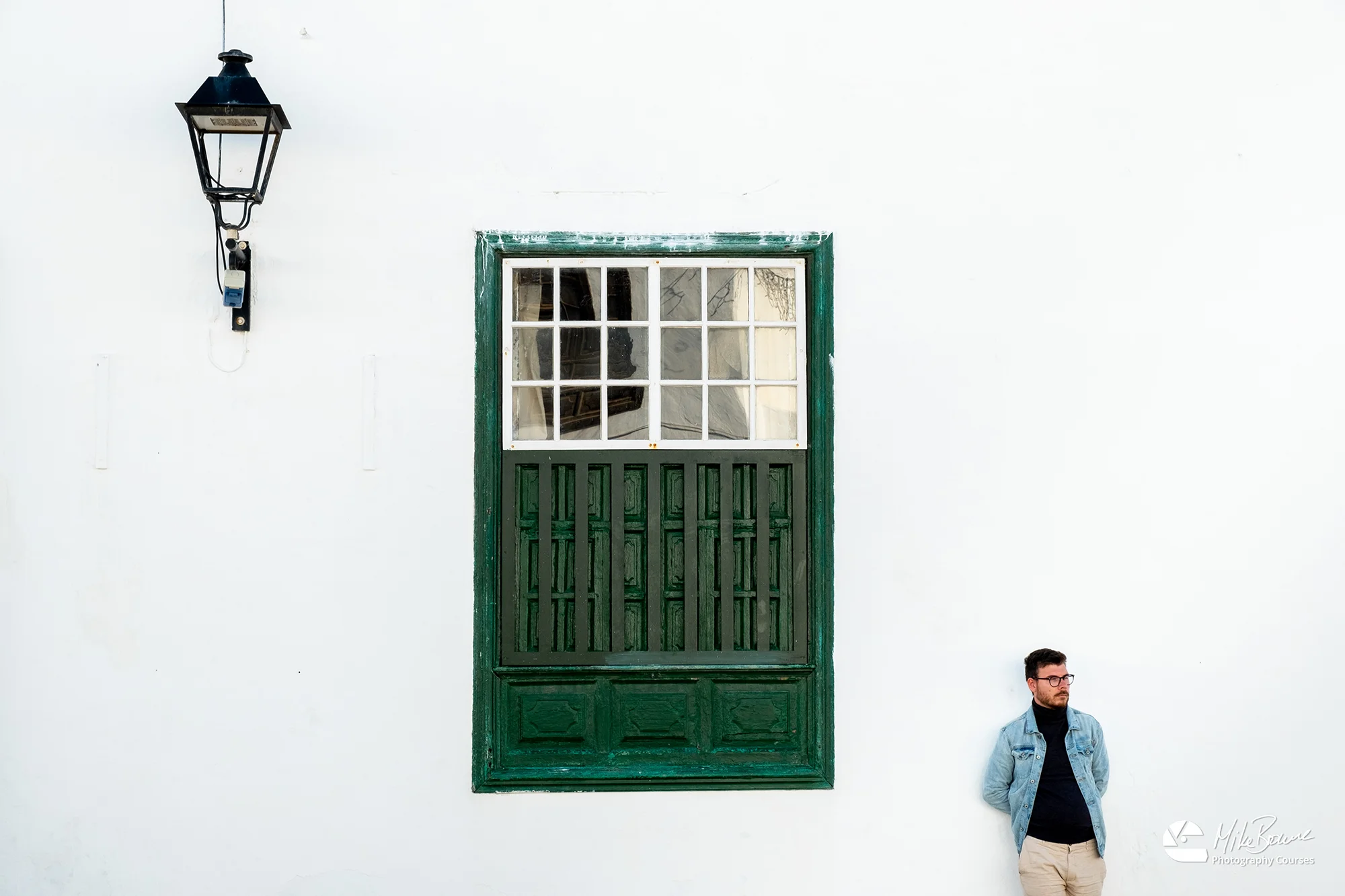 Man wearing glasses leaning against a white wall with green door in village on Lanzarote