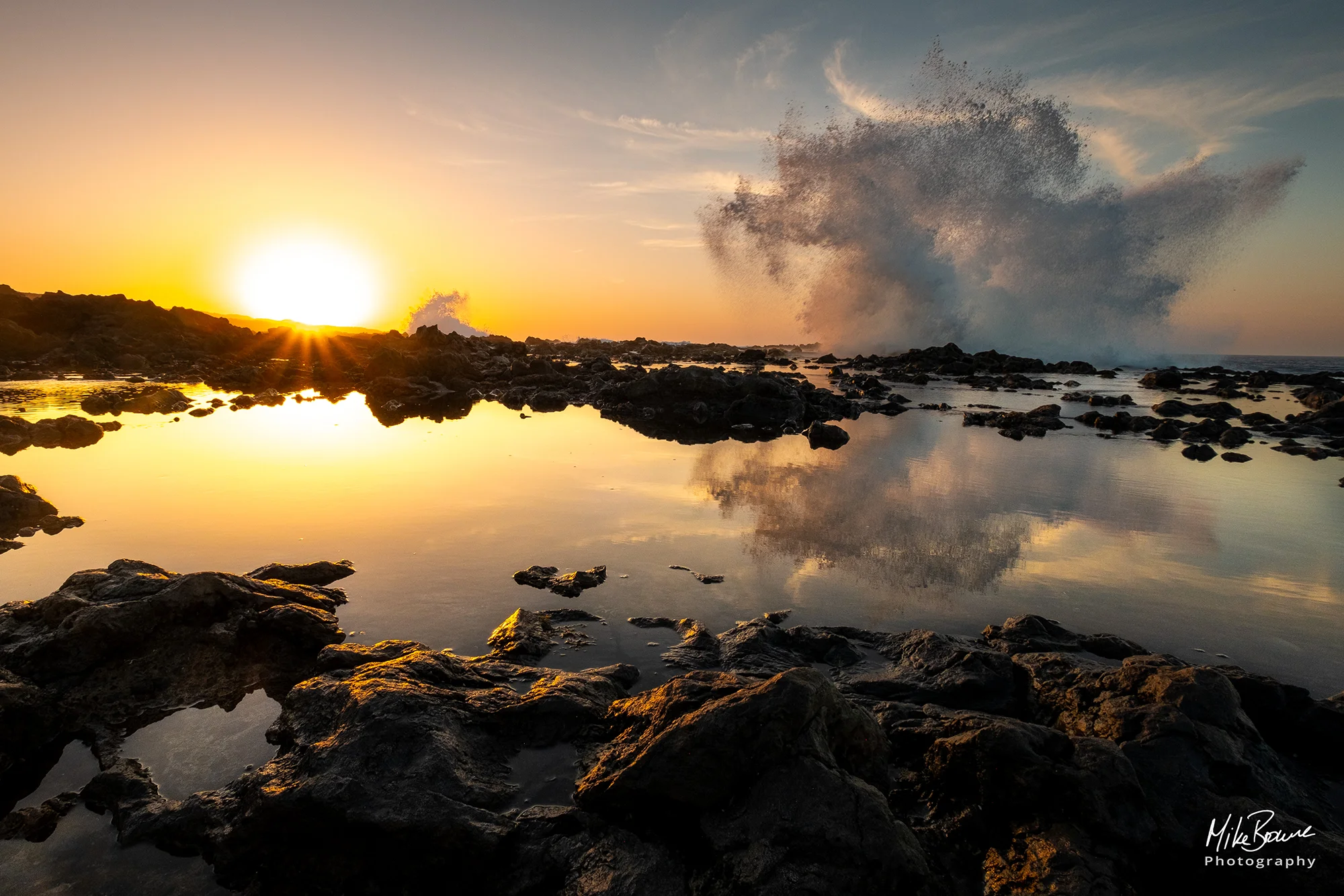 Sunset reflected in rock pool as a wave breaks over the rocks at Tenesera Lanzarote