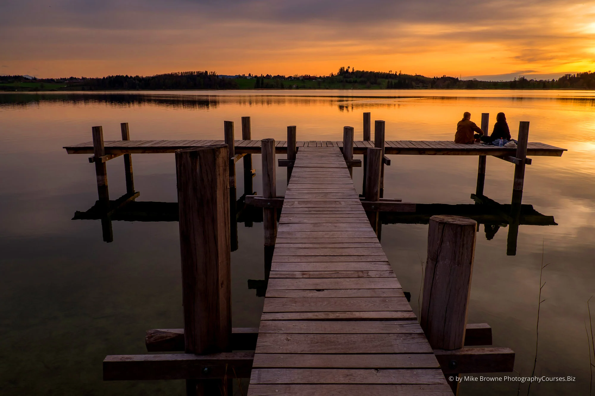 Two people sitting on a dock at Pfäffikersee watching sunset