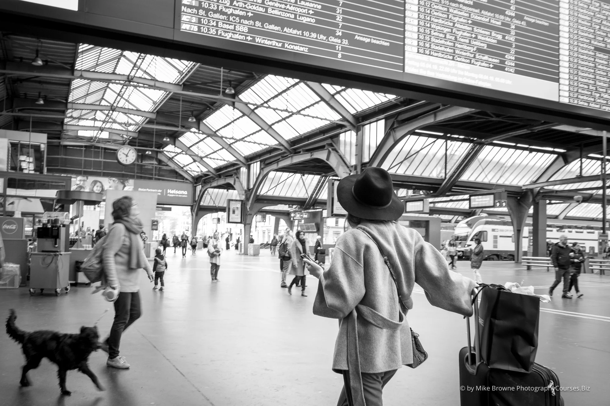 Rushing woman holding iphone in busy station glancing at giant timetable display at hauptbahnhof zürich