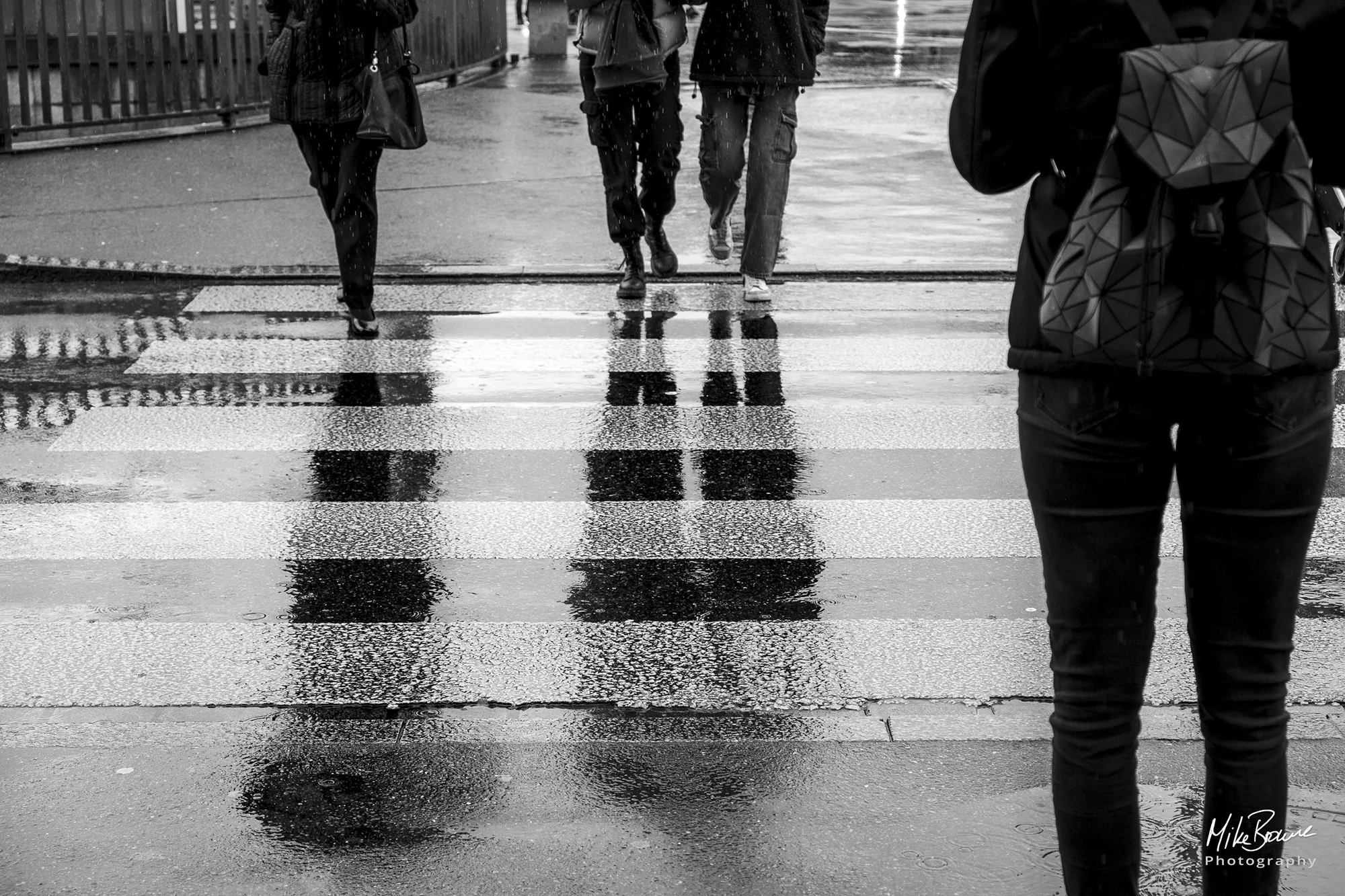Reflection on a wet road of of three people at a pedestrian crossing