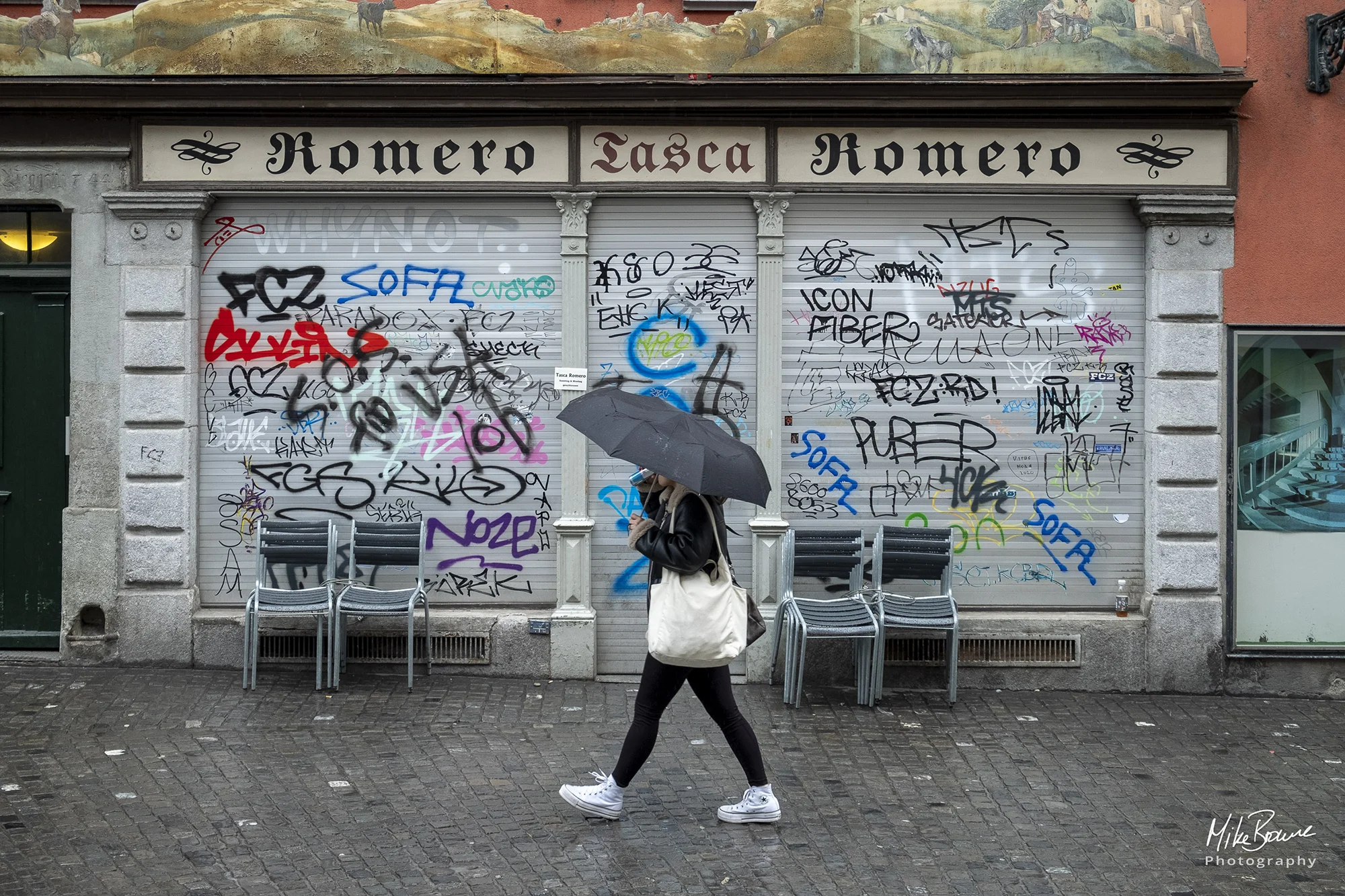 Woman with umbrella and shoulder bag walking past graffiti in Zurich