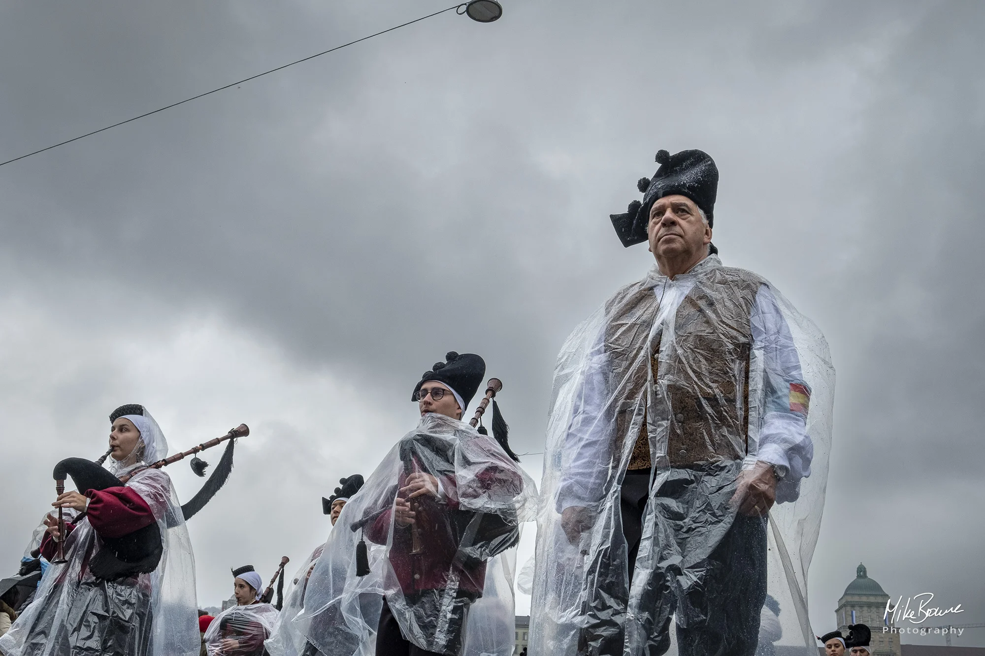 Two people playing bagpipes and a grim faced man in the rain at Sechseläuten parade