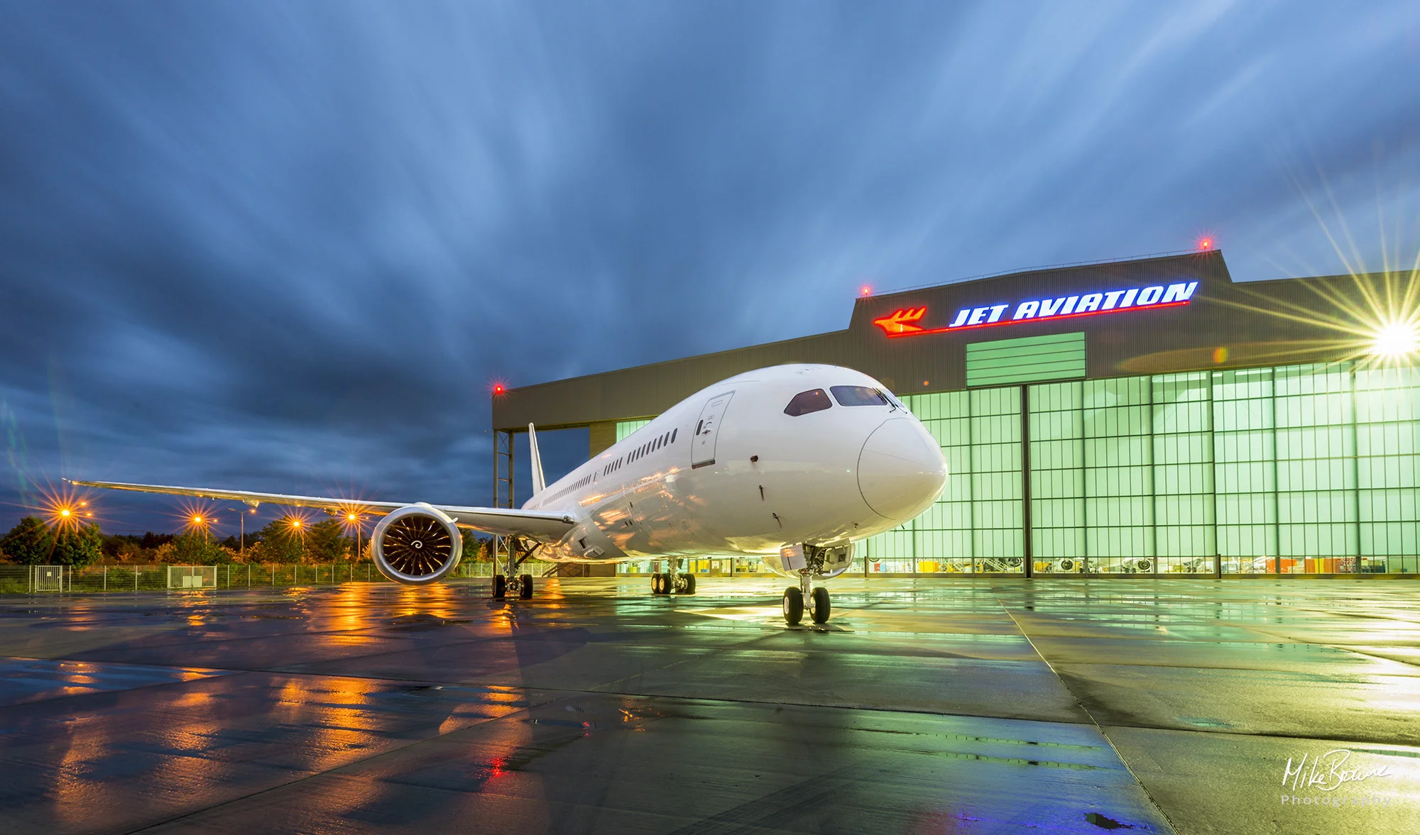 Floodlit Boeing aircraft and it\'s reflection on wet concrete at night