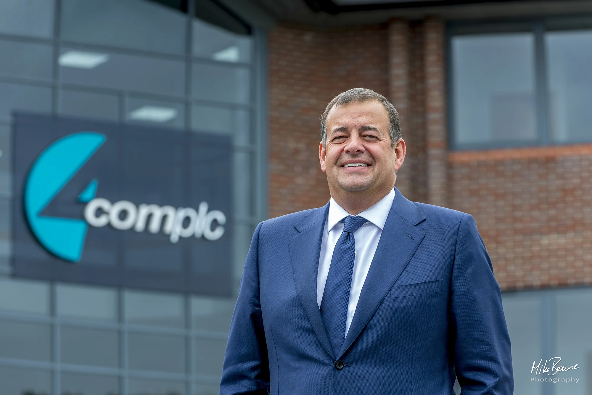 Businessman wearing a suit with company signage on wall behind him