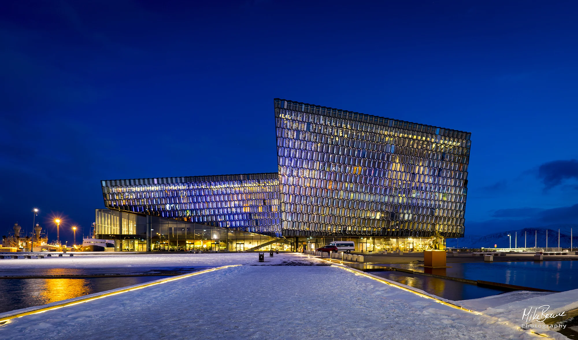 Harpa concert hall in Reykjavik, Iceland with blue twilight sky and snow on footpath to entrance