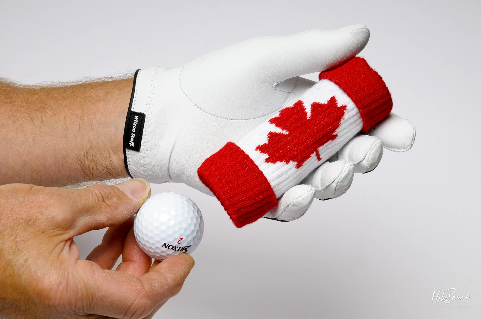 Man\'s hands with white glove inserting a golf ball into a holder bearing Canadian flag logo