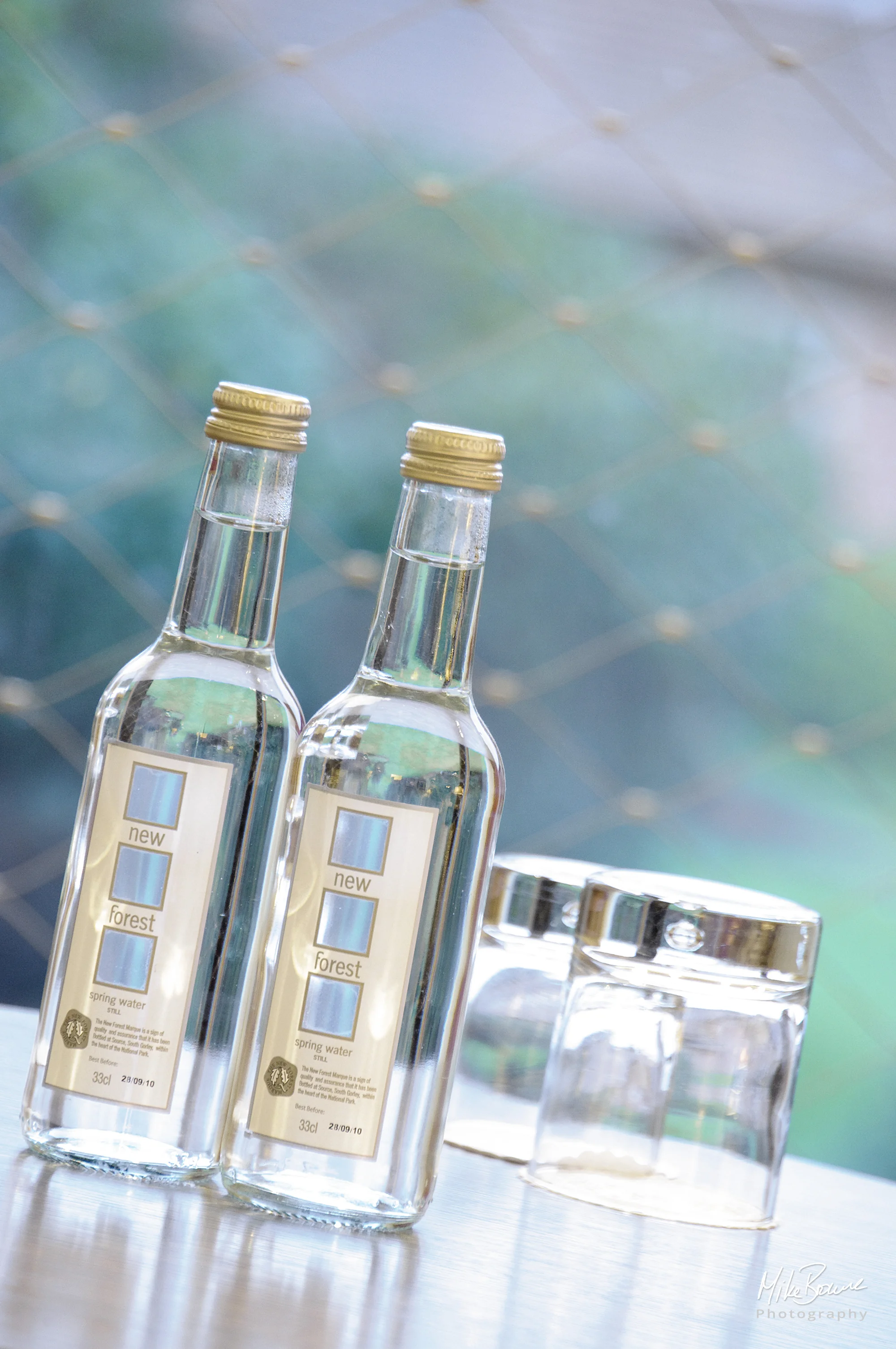 Two bottles of mineral water and glasses with window in background