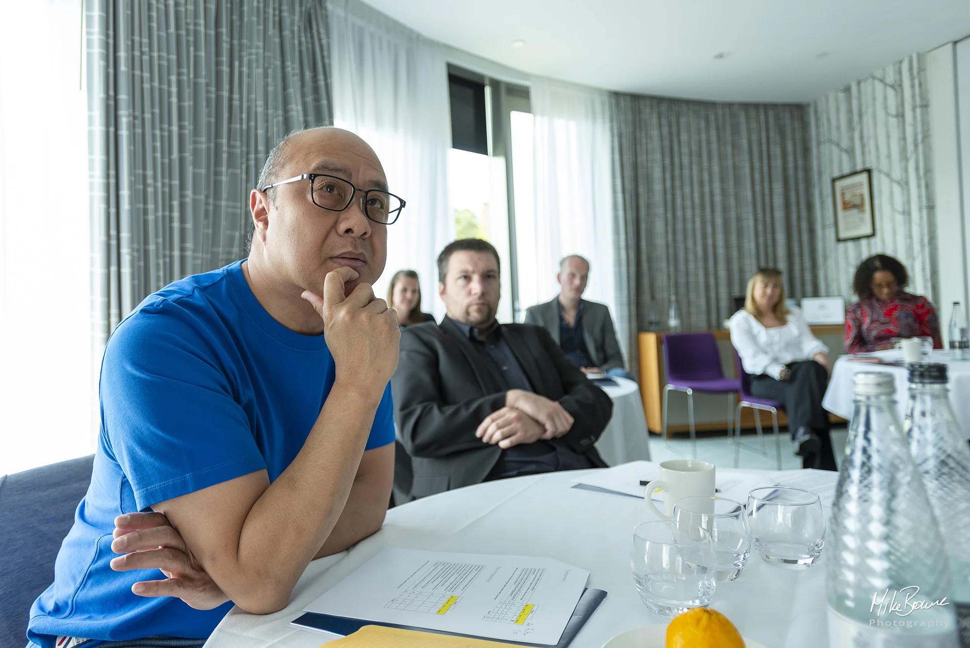 Man wearing glasses with look of concentration in a room of business people during a presentation