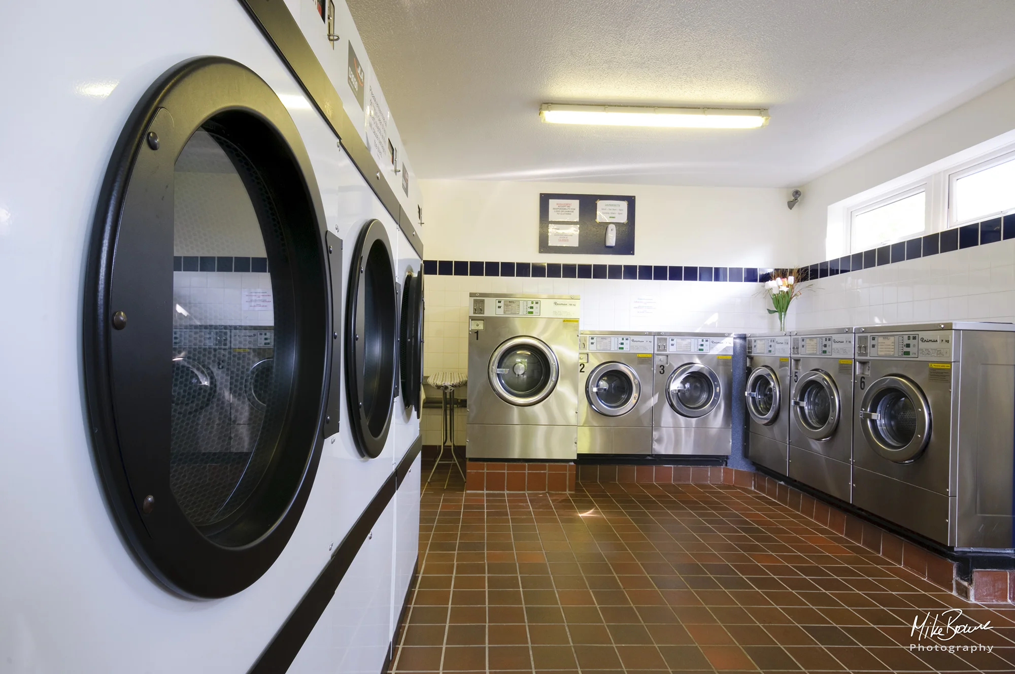 Commercial washing machines and dryers in a commercial laundry with brown tiled floor