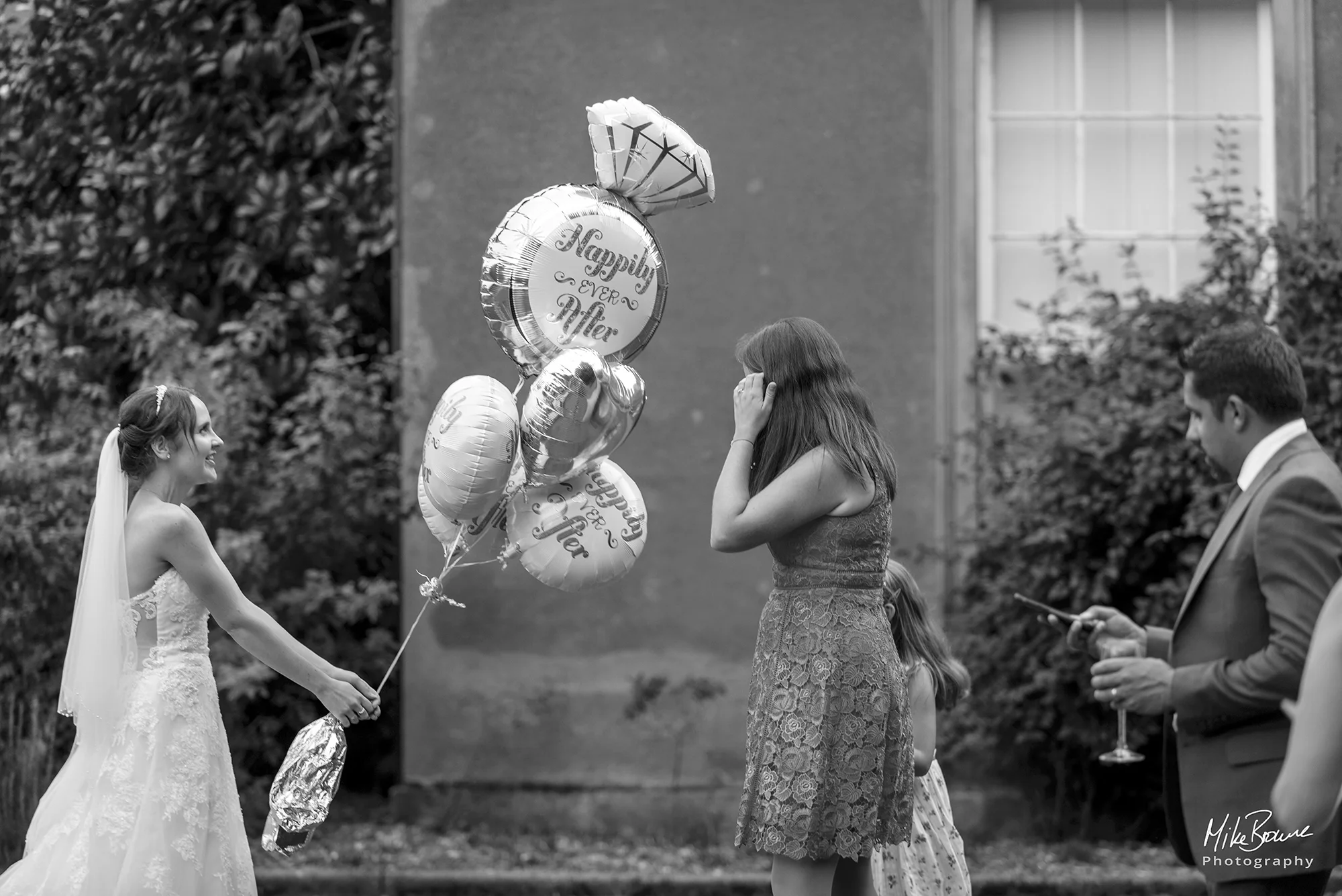 A bride holding bunch of balloons with Happily Ever After written on them