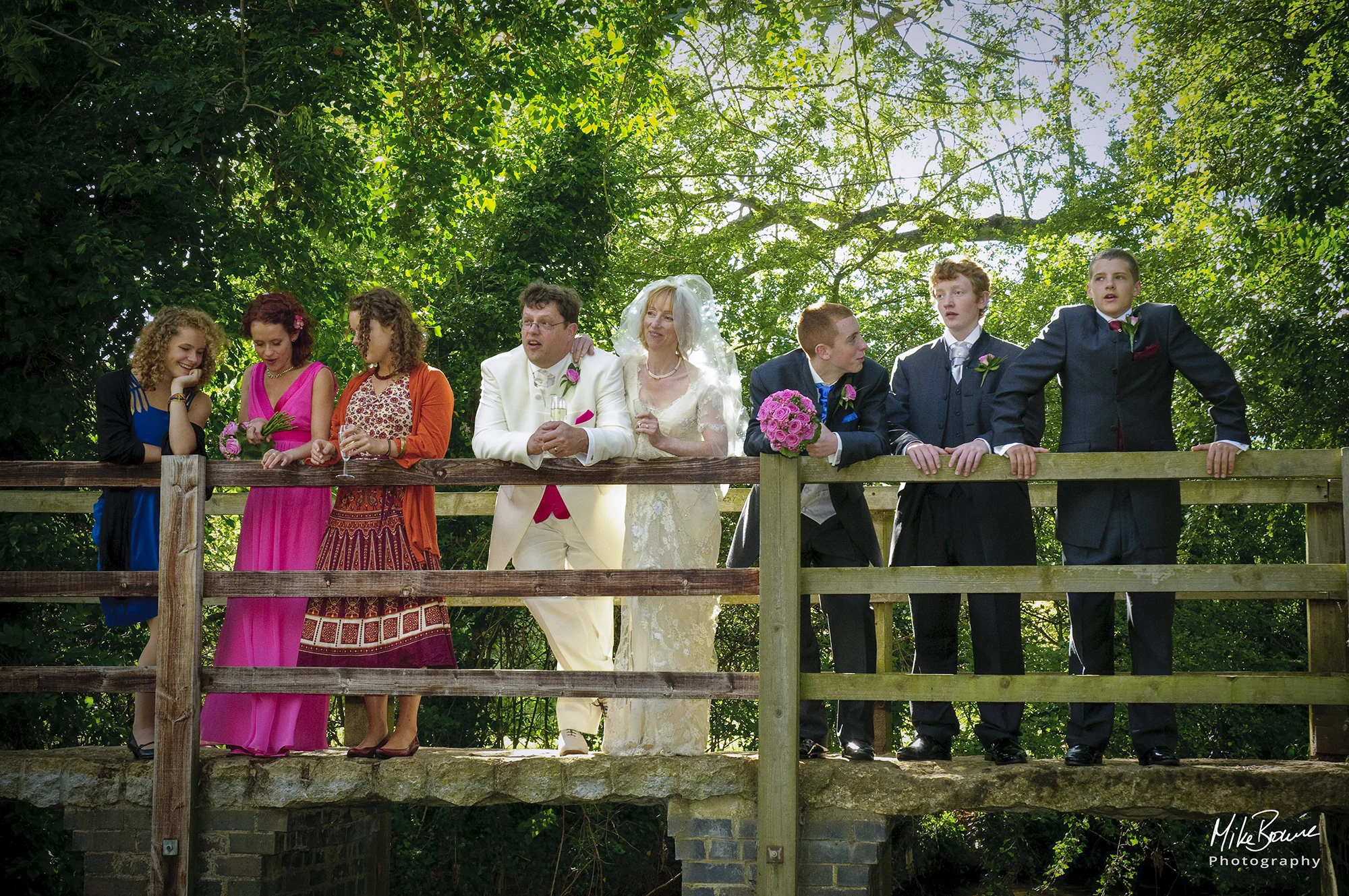 Wedding couple with bridesmaids an ushers talking on a bridge in a forest