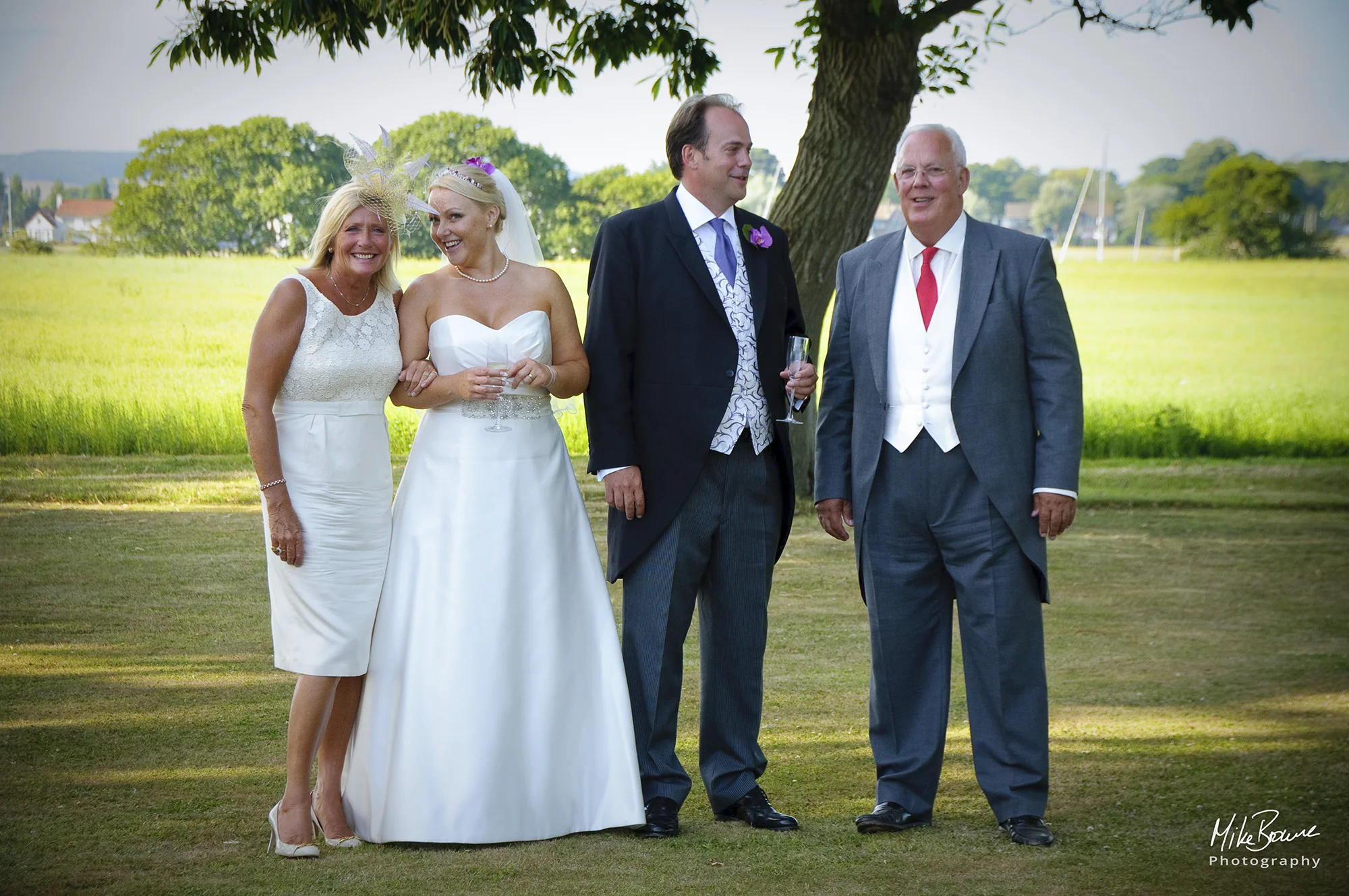 A young Bride and Groom smiling as they talk with an older couple with green fields beyond