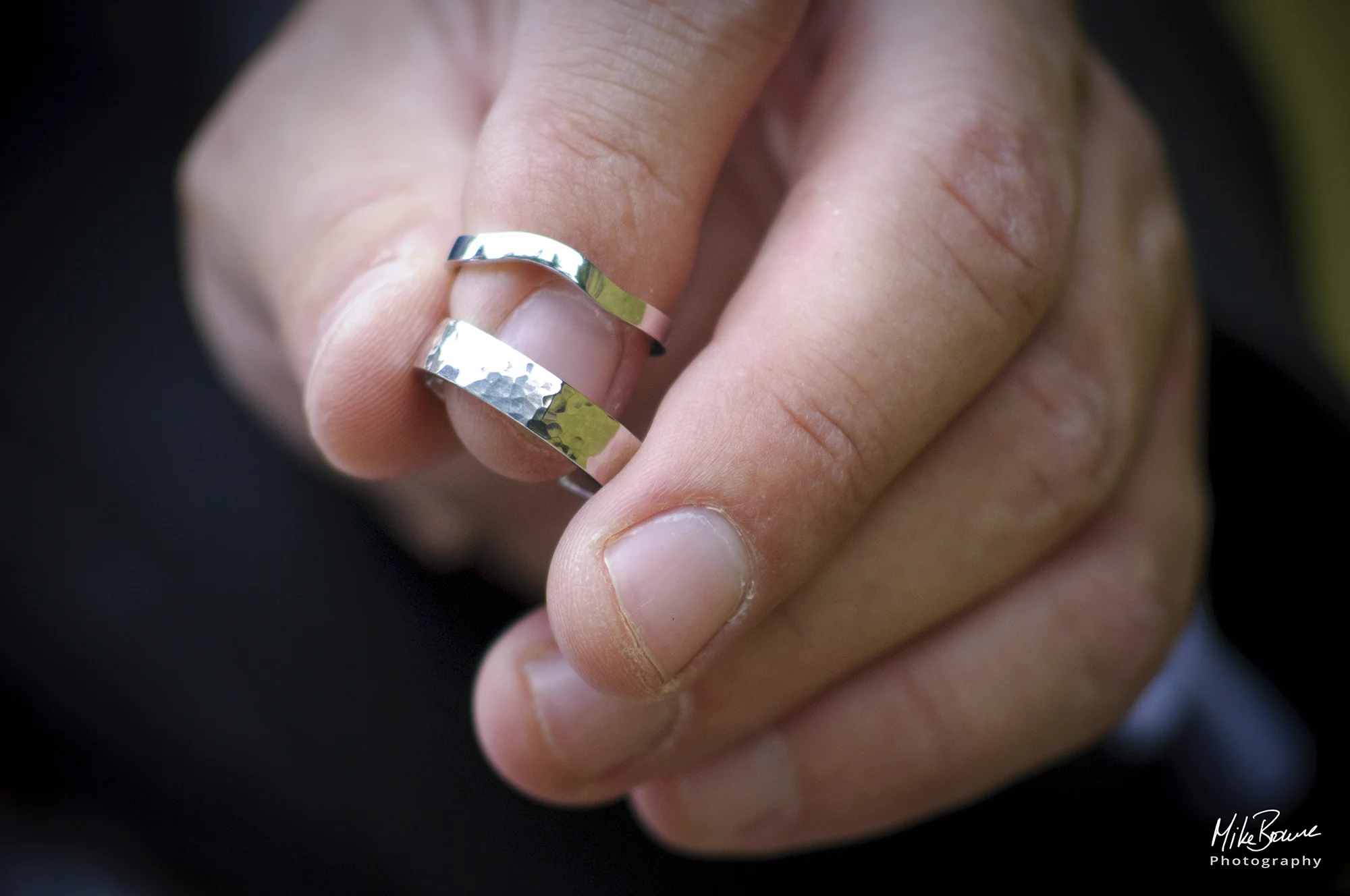 A man\'s left hand with two wedding rings on the tip of the index finger