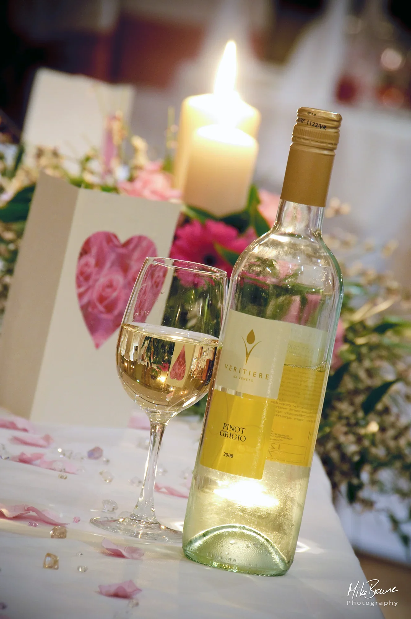 Bottle and glass of white wine on a table with flowers, candles and a card with a heart