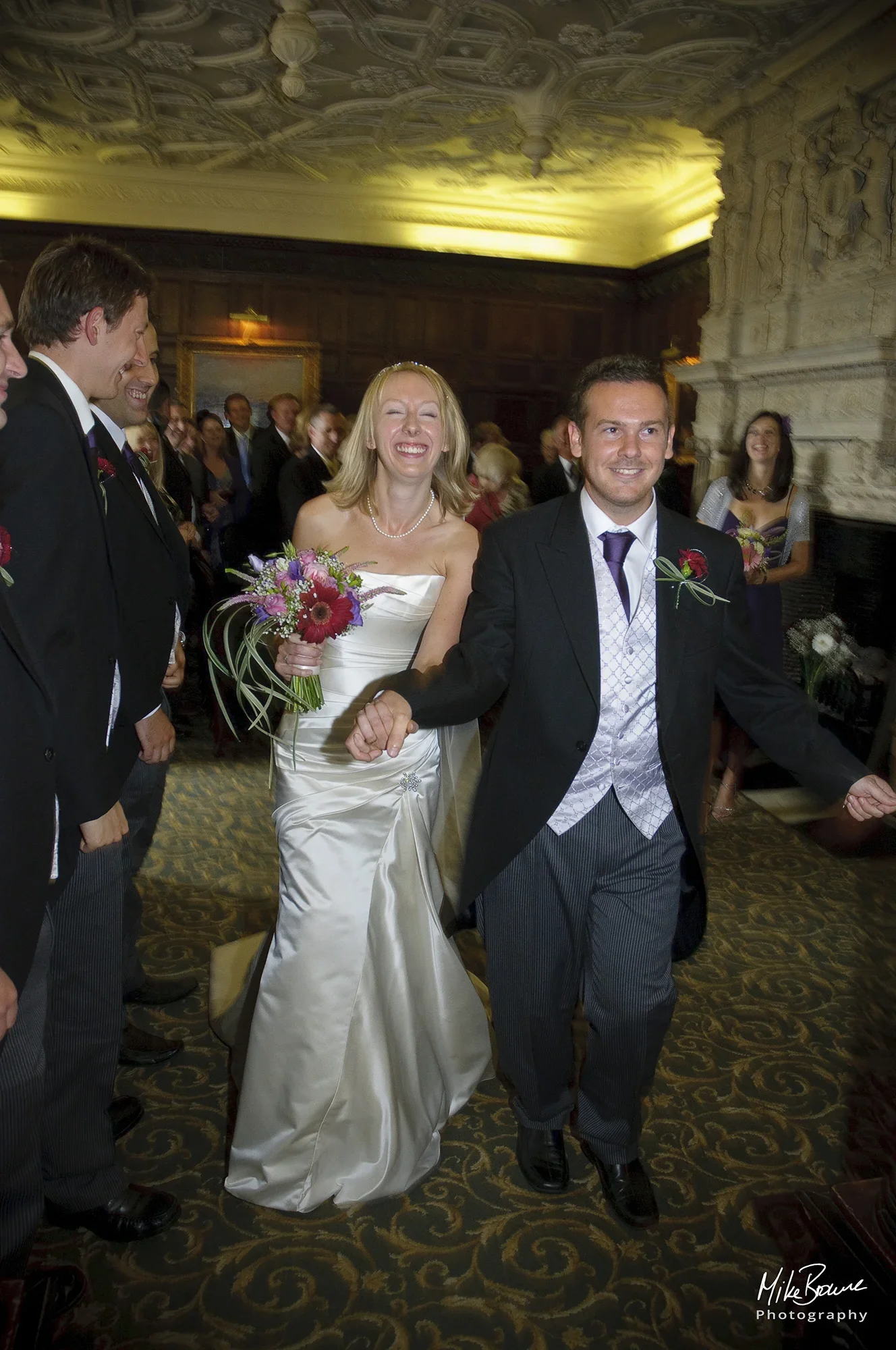 Newly weds walking down the aisle in an ornately panelled wedding venue with huge smiles on their faces