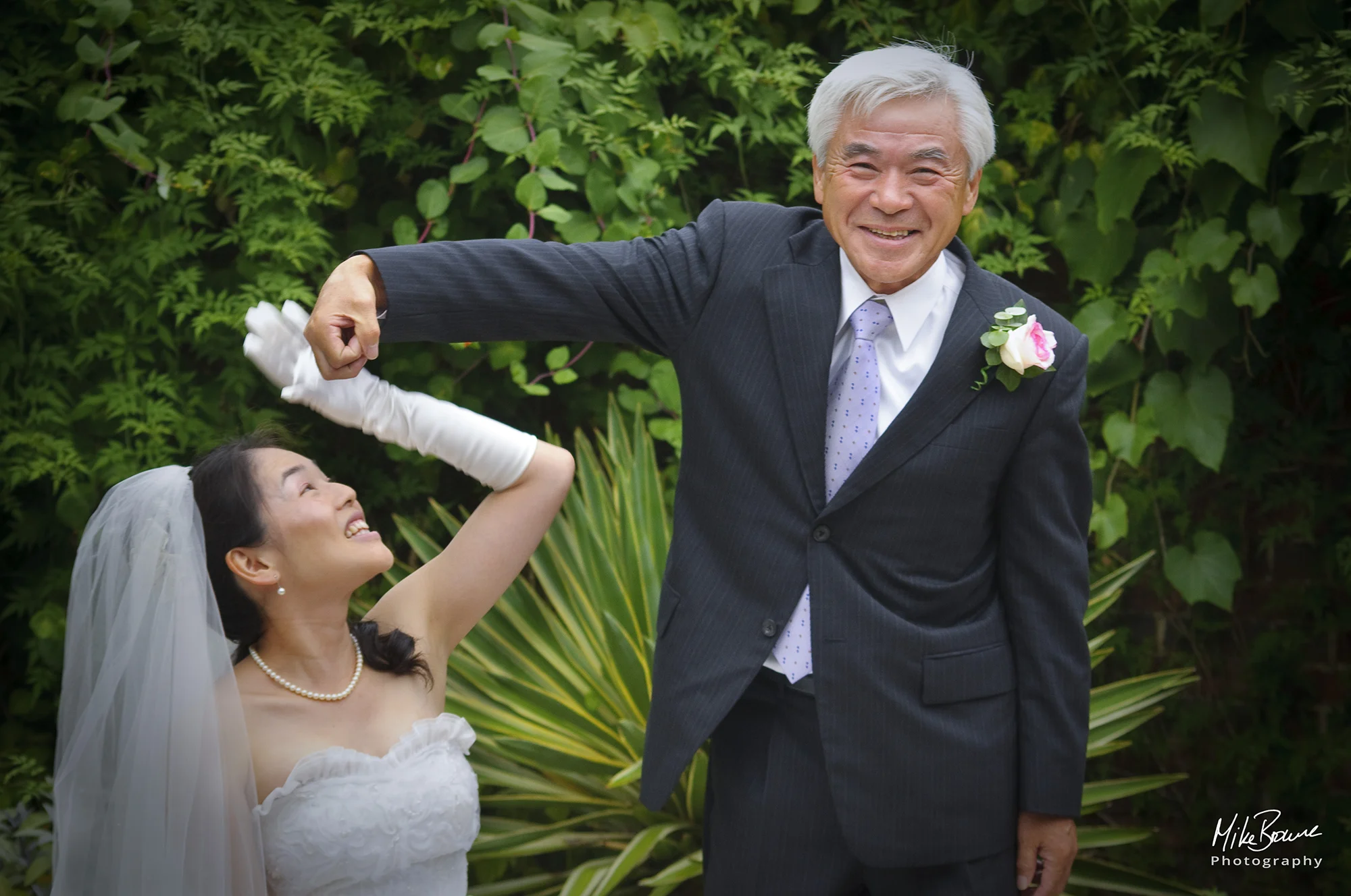 Smiling father of the bride wearing pinstripe suit and pink rose joking with his daughter the Bride