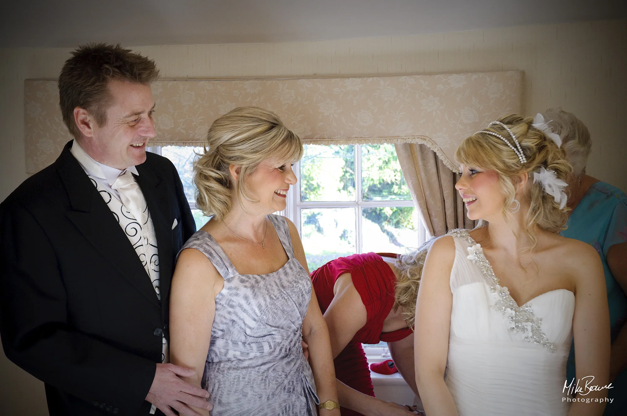 Mother and father of a bride looking at her as she is fitted into her wedding dress