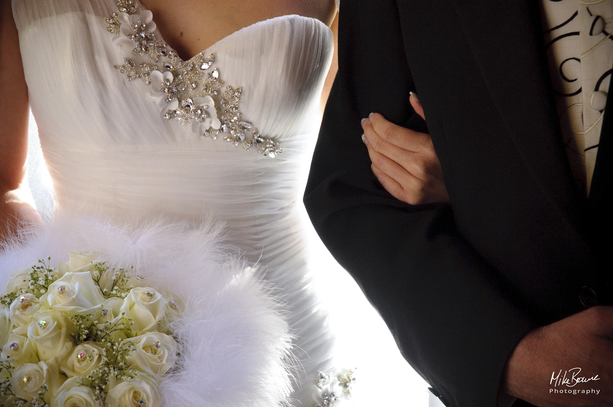 Details of a bride\'s dress and flowers as she holds her father\'s arm