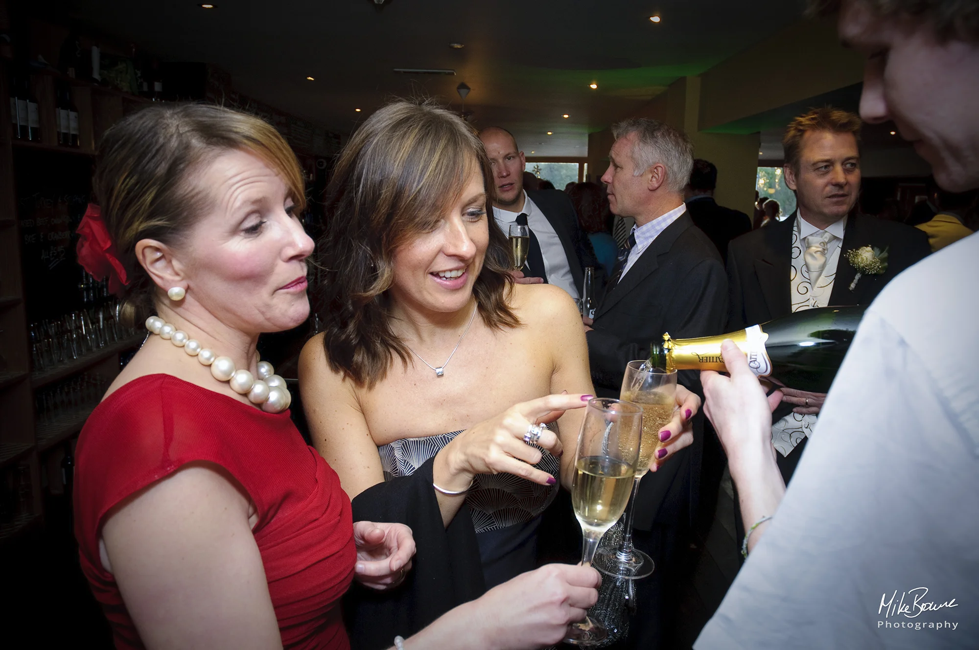 Two female wedding guests having their glasses refilled with Champaign at a reception