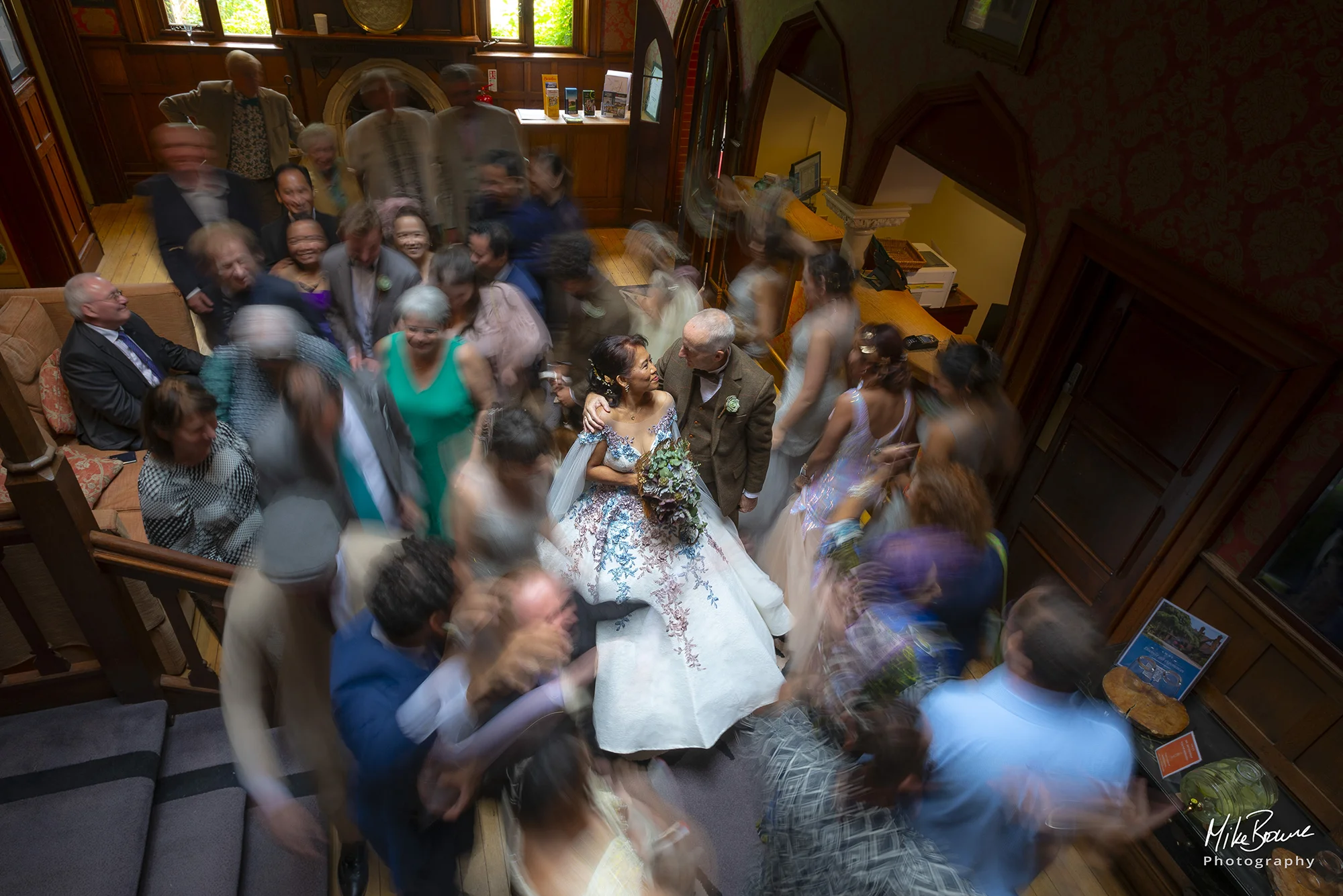 A Bride and Groom gaze into each other\'s eyes as guests swirl about them in a hotel foyer