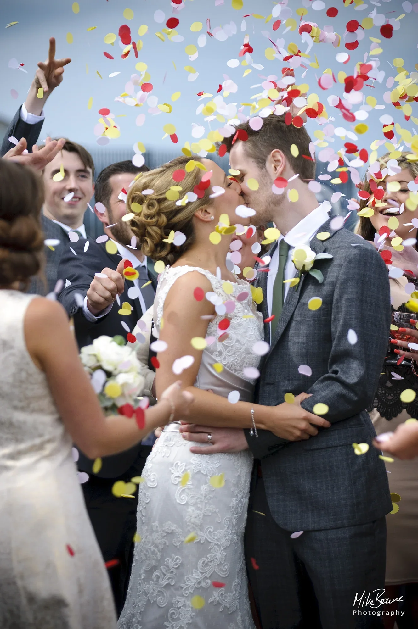 A young couple kiss as friends and family throw confetti in the air around them