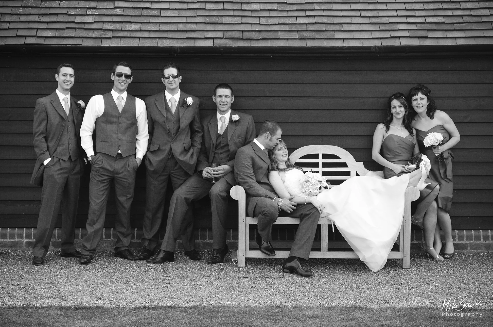 Bride and groom on a wooden bench with their bridesmaids and ushers