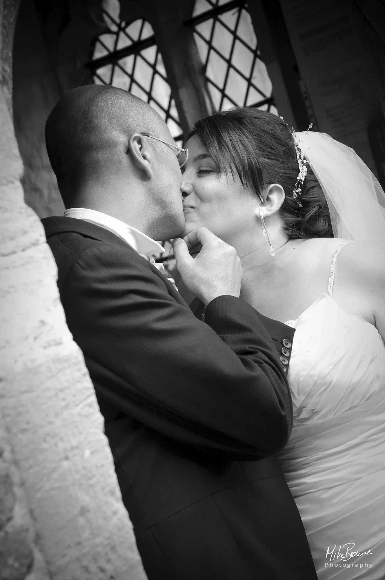 Man in a morning suit caressing the face of a woman wearing a wedding dress as he kisses her on the lips