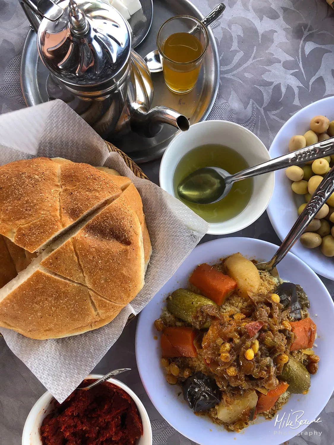 Traditional Moroccan food of unleavened bread, olive oil, mixed vegetables, green olives and a silver pot of tea