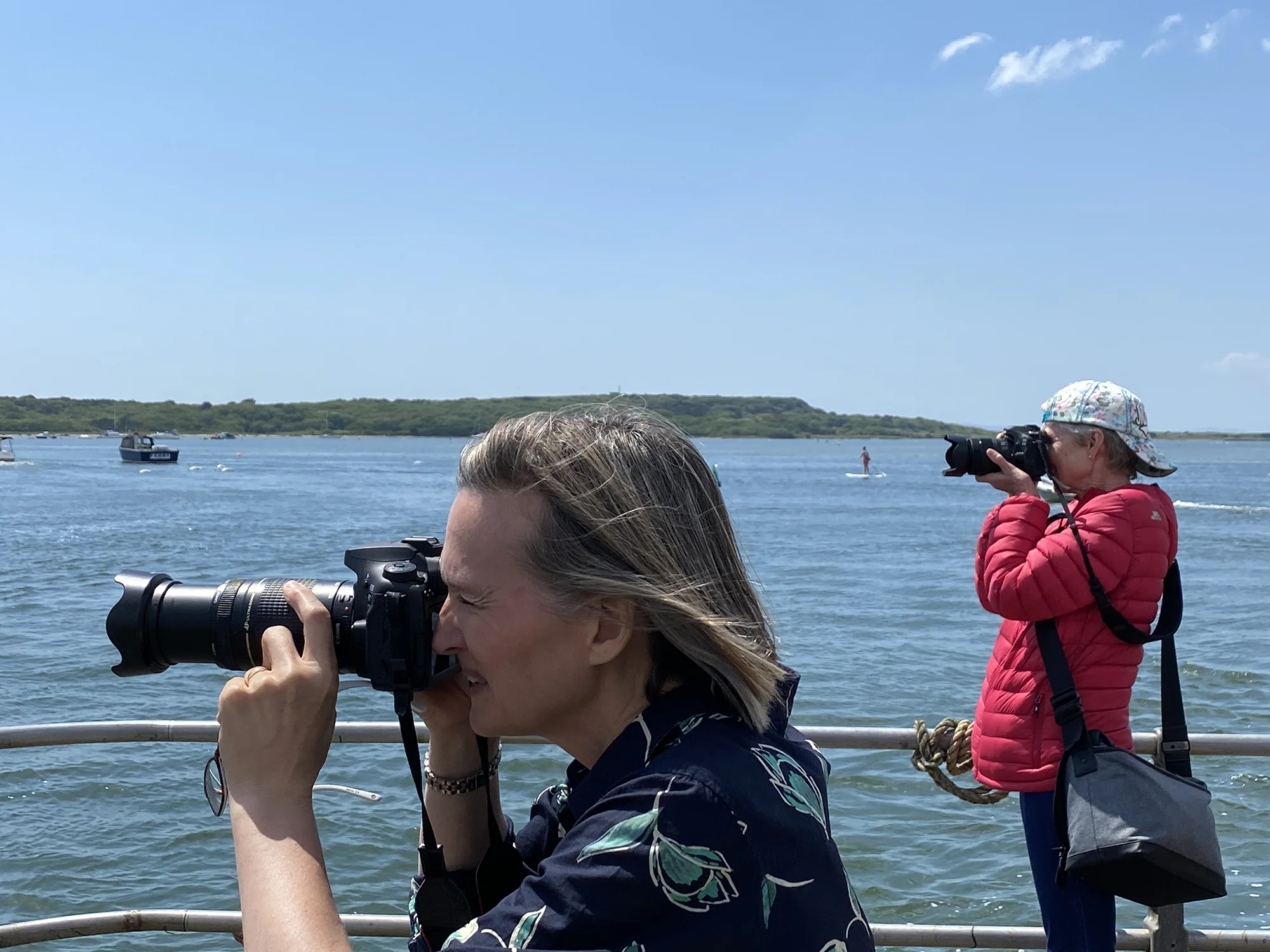 Two female photographers with cameras raised standing by the water at Christchurch harbour UK