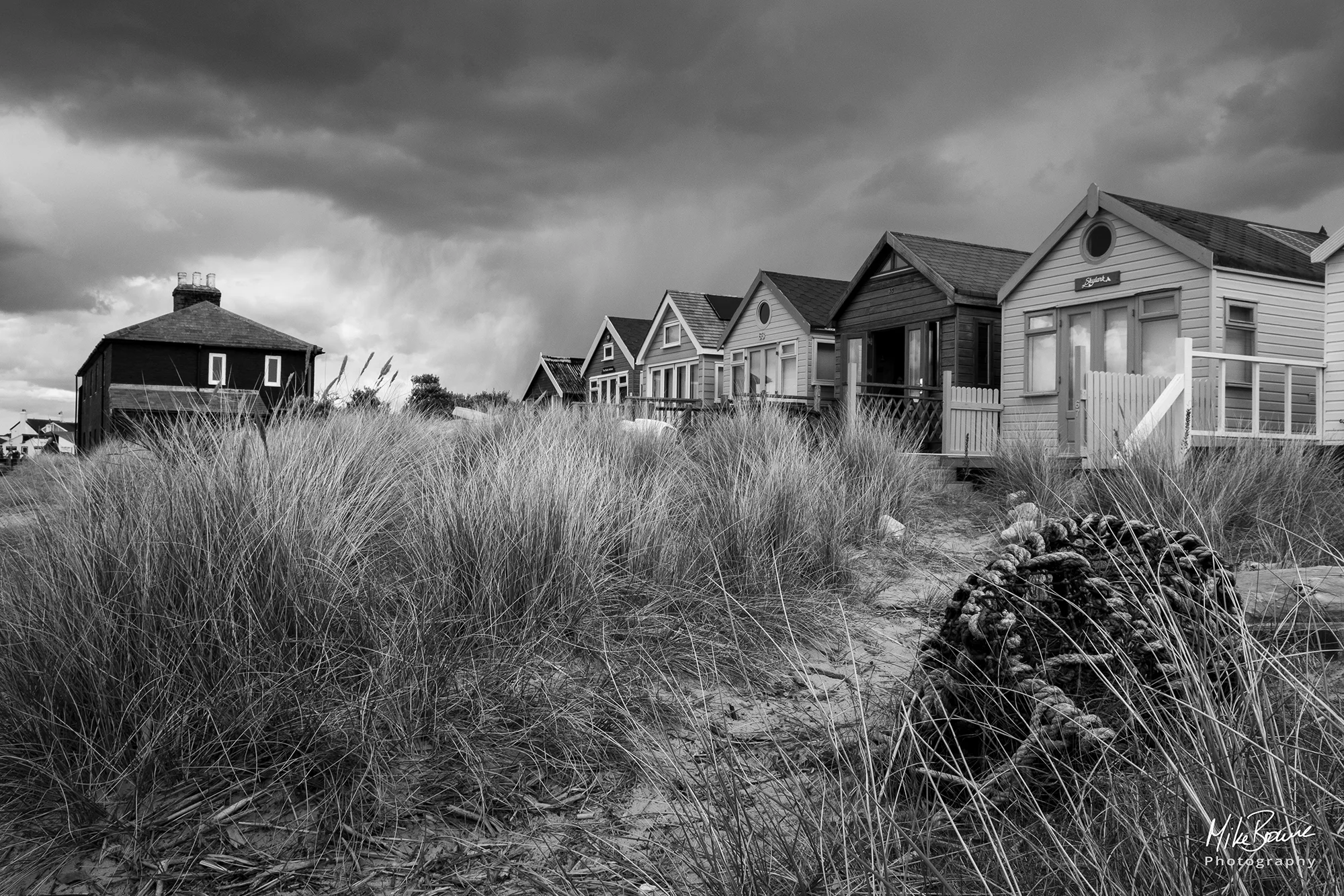 Lobster pot and grasses in front of beach huts with storm clouds in sky