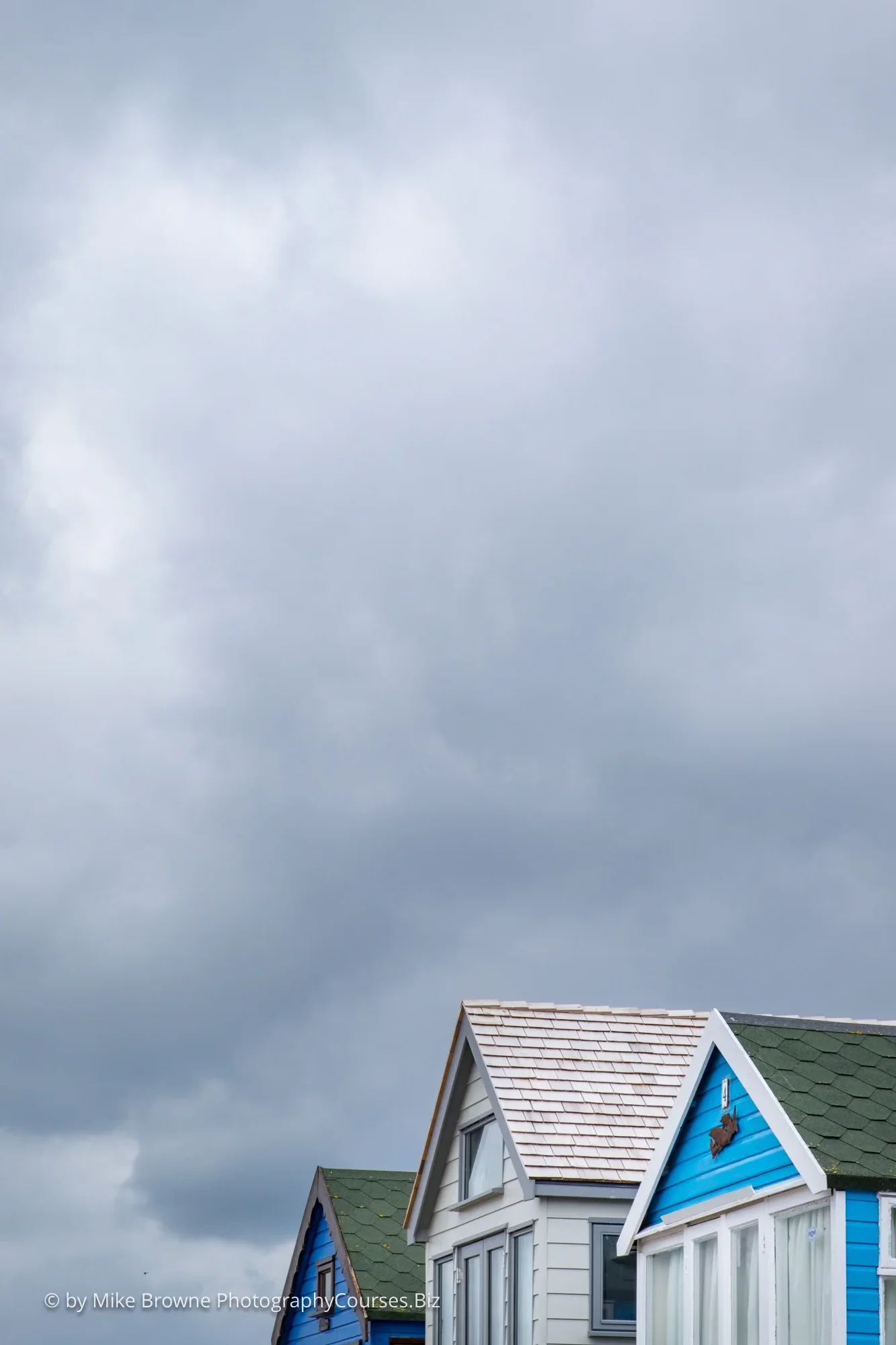slanting roofs of three beach huts against cloudy sky
