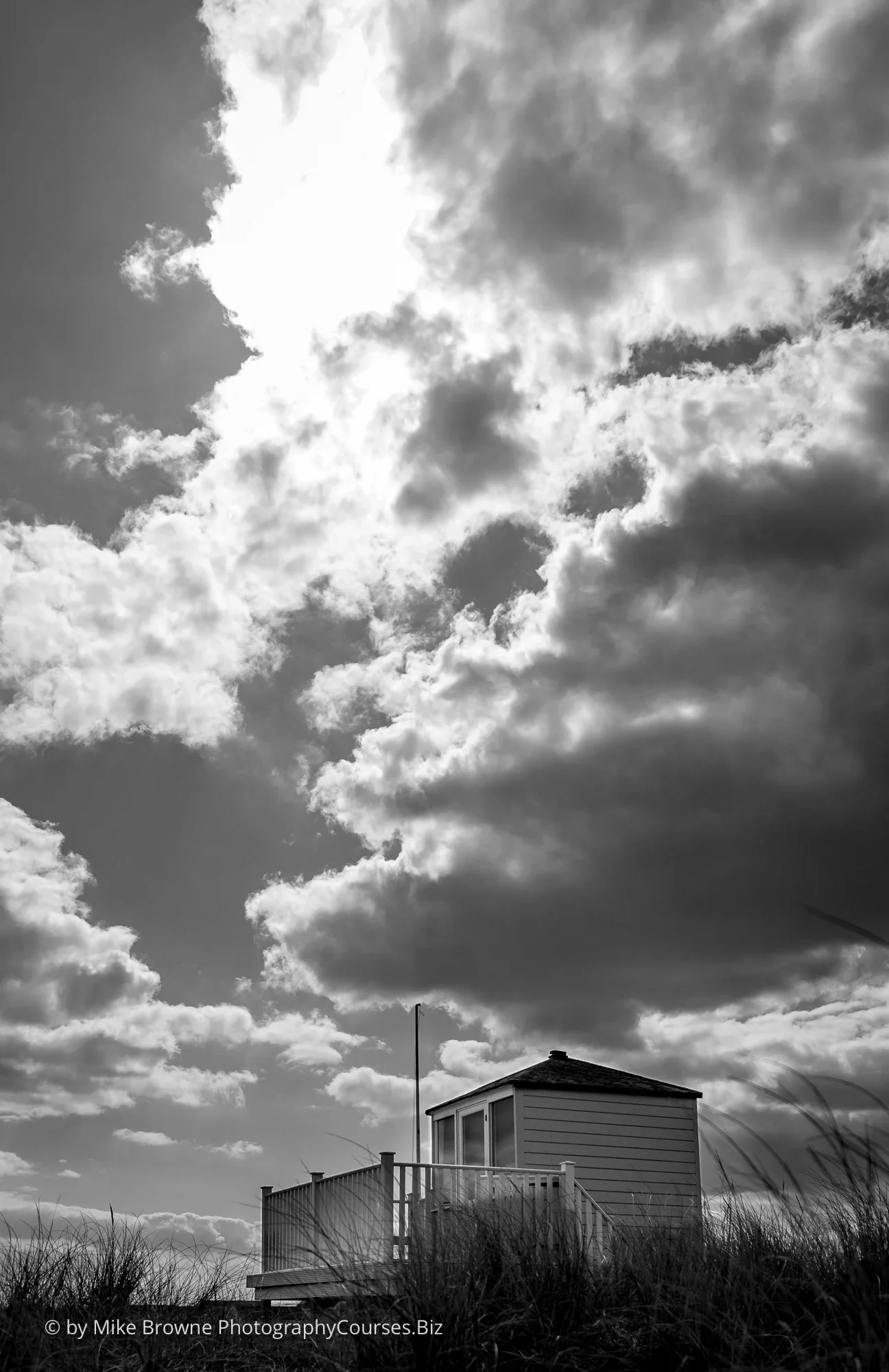 Summer sky with sun and clouds above a lone British beach hut