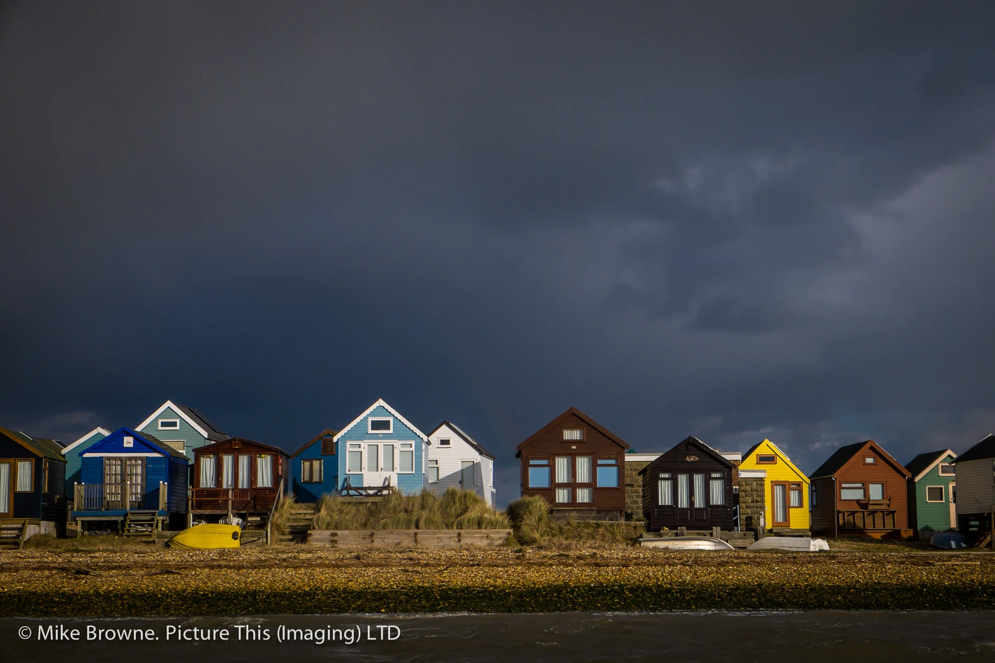 Row of colourful British beach huts under heavy storm clouds