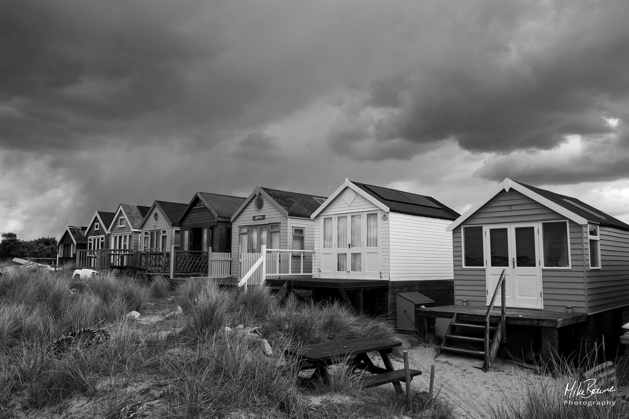 British beach huts and long grasses under heavy storm clouds