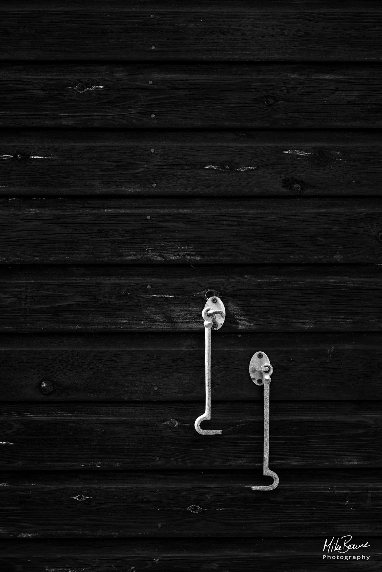 Two metal hooks mounted on a black painted wooden wall