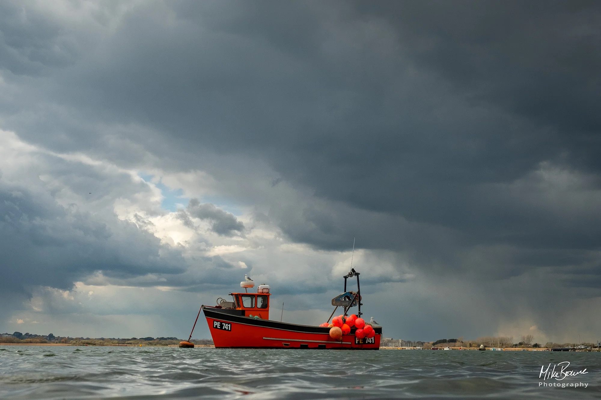 Orange fishing boat on calm water on a cloudy day