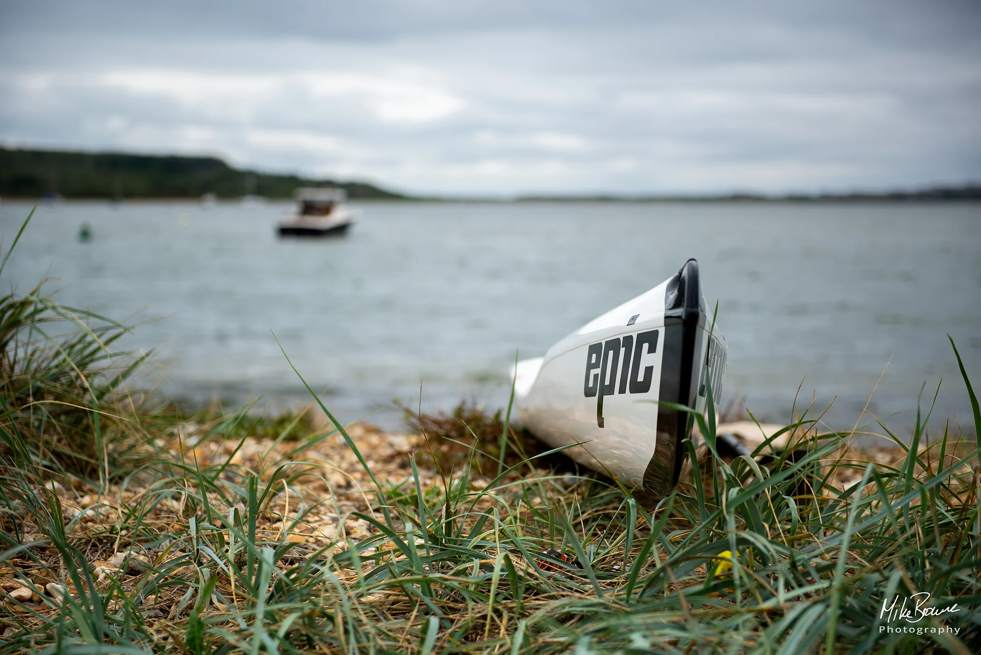 Racing canoe with word \'Epic\' painted on it pulled up on shore of a small harbour