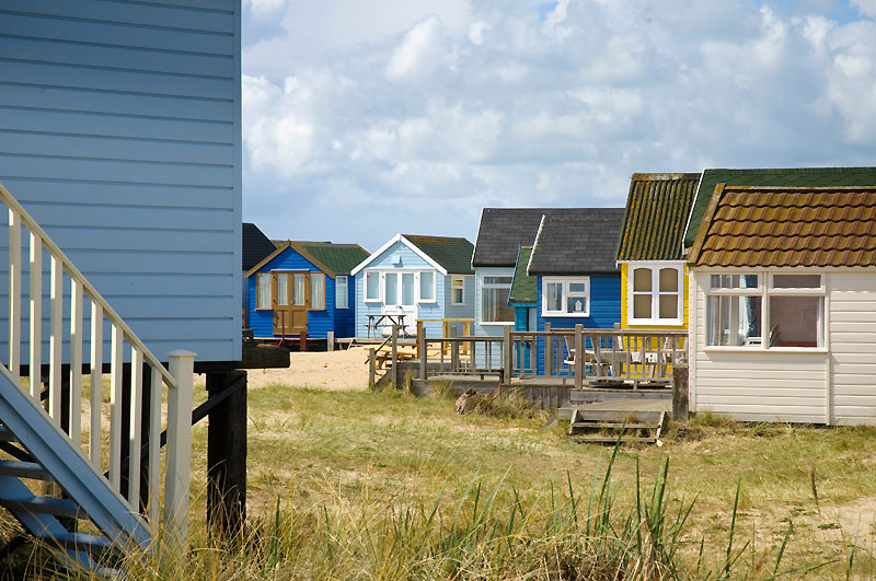 Higgledy piggledy beach huts with grass in the middle and a cloudy sky