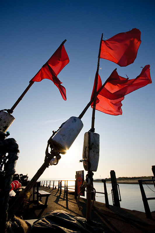 Bright red flags on three poles blowing in the wind against blue sky