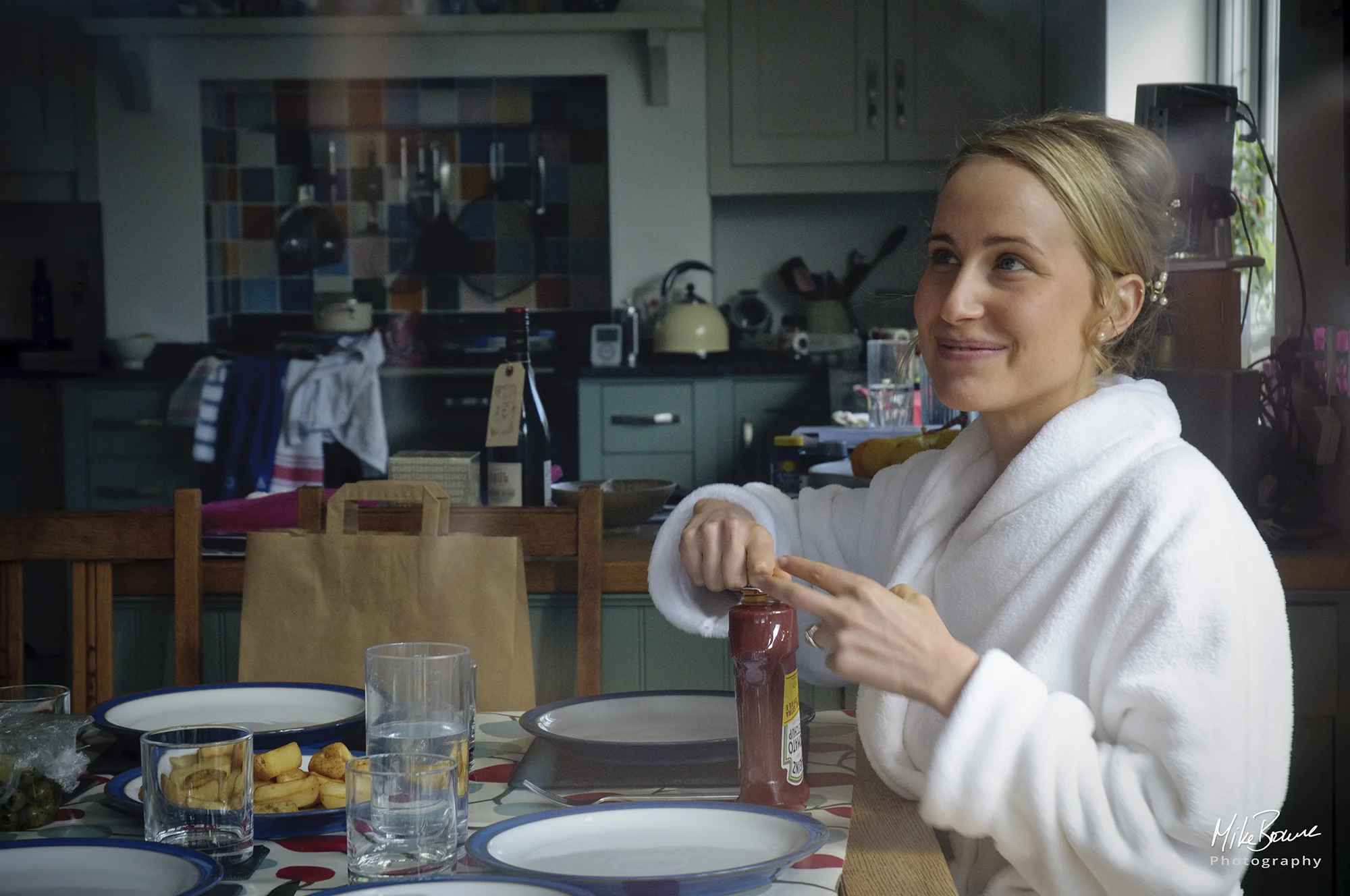 Smiling young woman with beautifully made up hair and wearing a white bathrobe sitting at a breakfast table